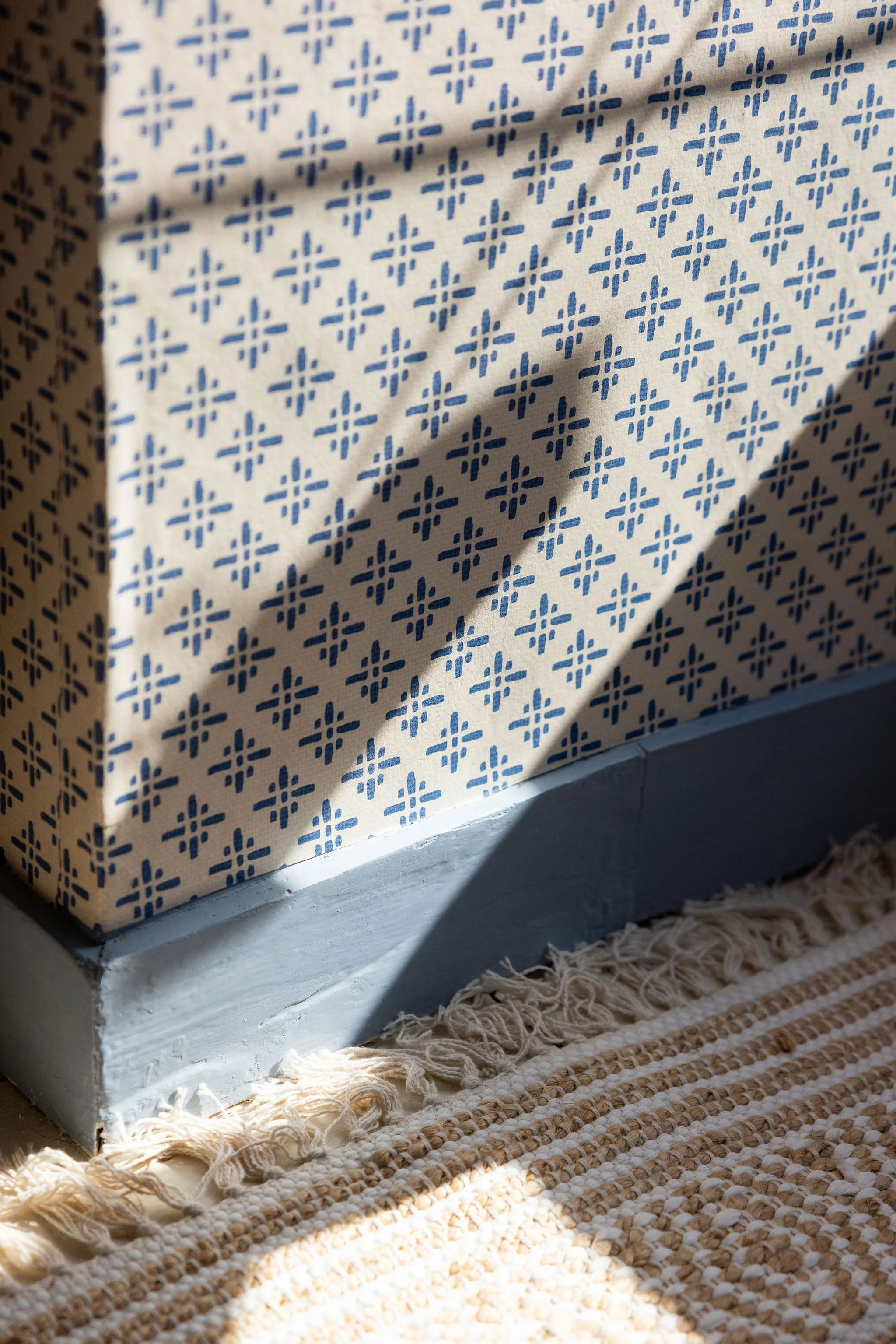 Close-up of a patterned cardboard box sitting on a textured rug near a window with sunlight casting shadows