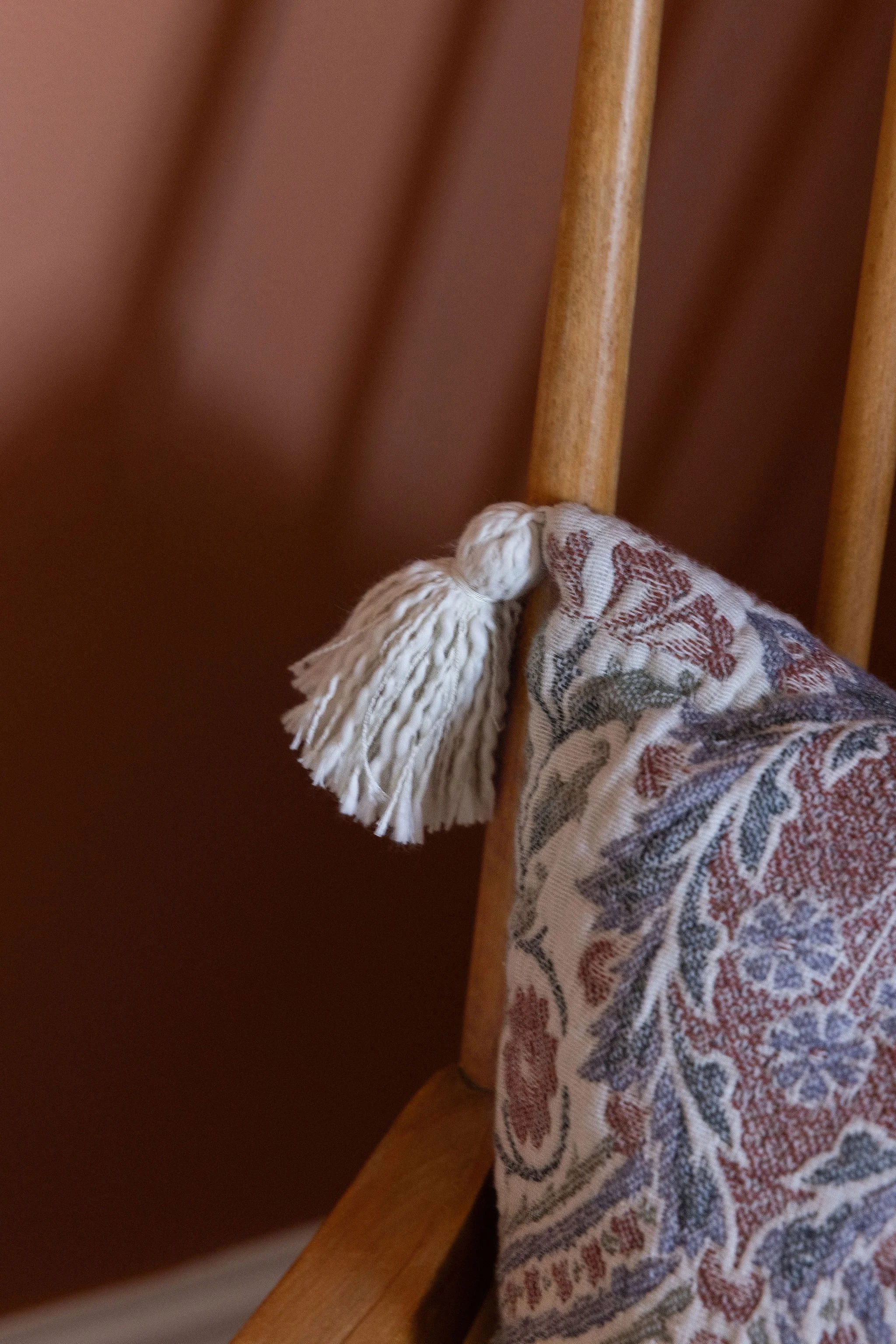 Close-up of a person's foot wearing a fringed sock, resting on the wooden support of a chair next to a wooden table or board.