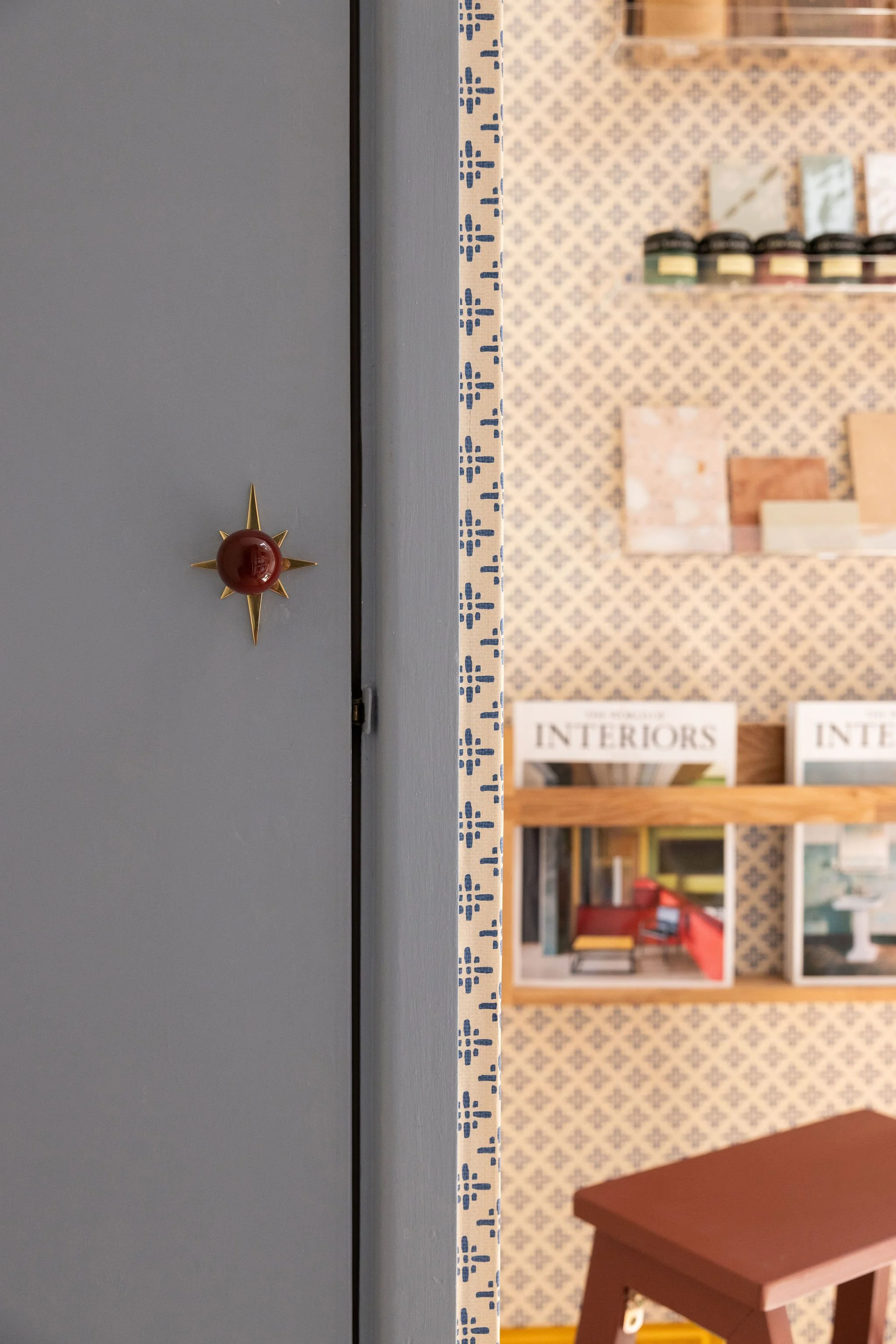 Part of a b lue door with a decorative knob on a wall, with shelves filled with books and decor items in the background.