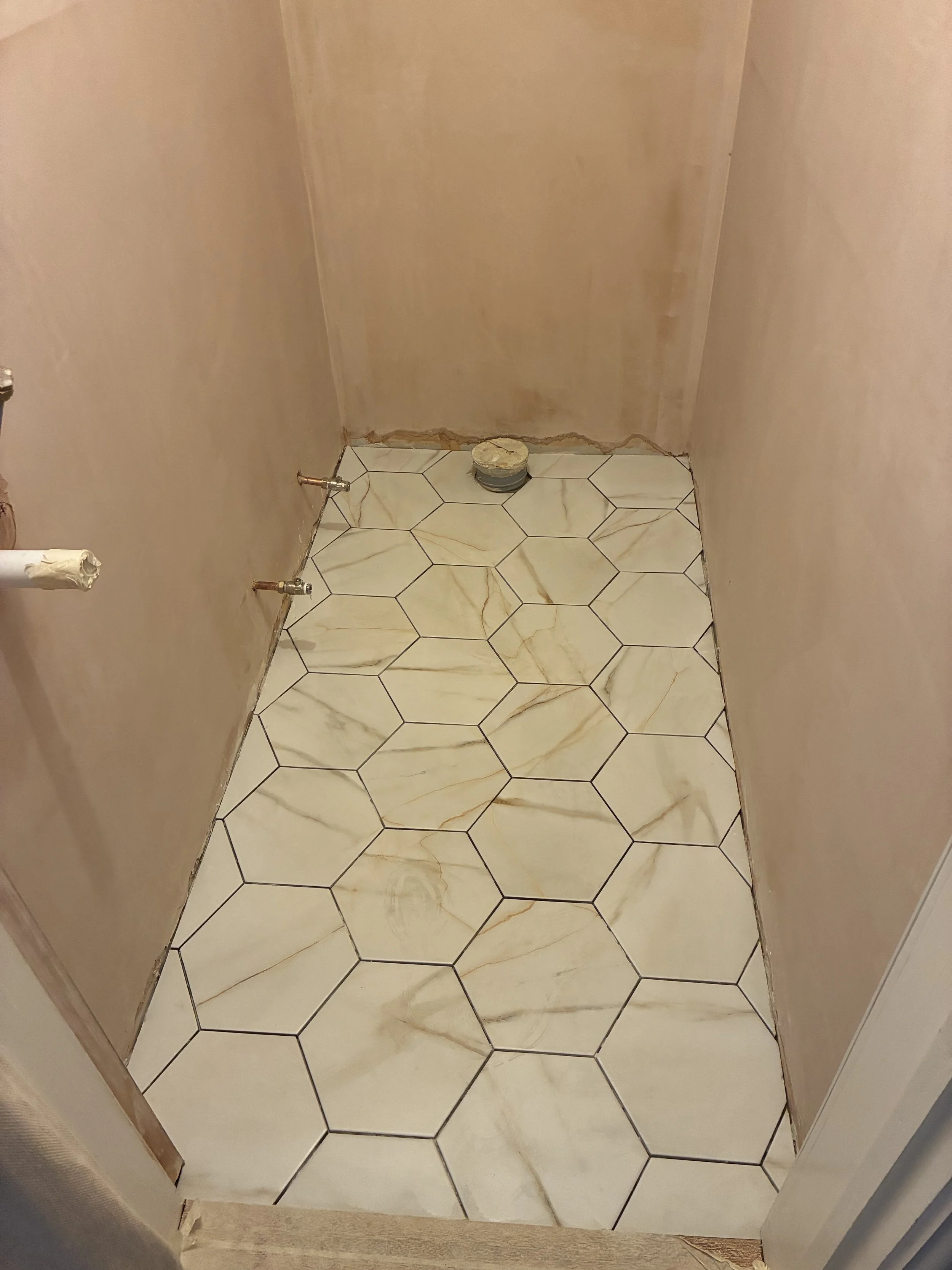Corner of a bathroom with beige walls, tiled marble floor, and plumbing fixtures.