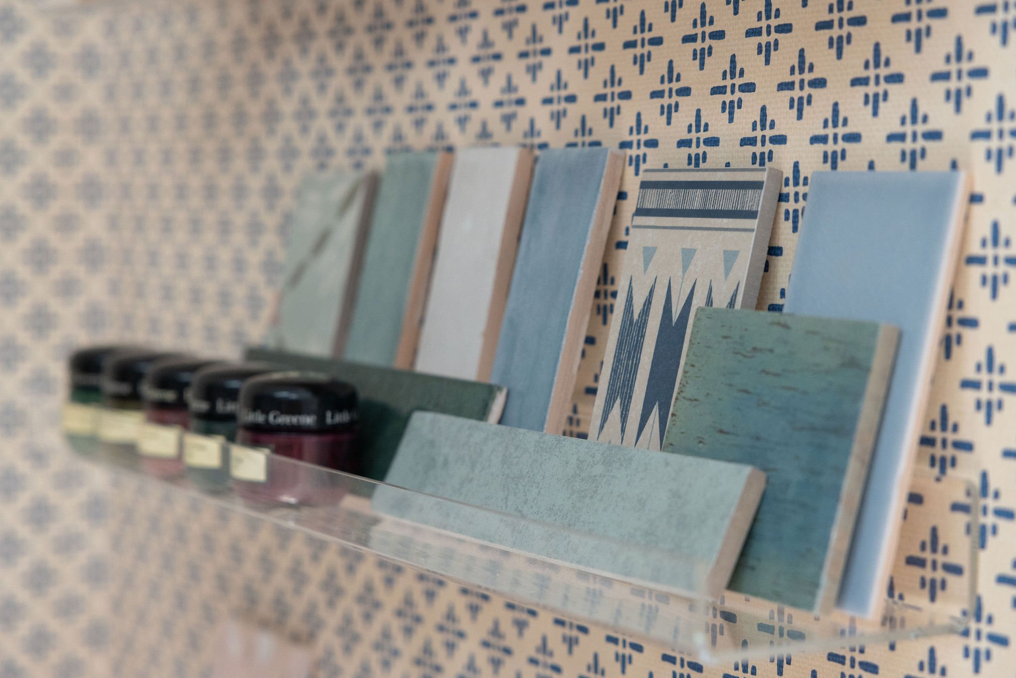 Close-up of a retail shelf with books and ink bottles against a blue and white patterned wallpaper background.