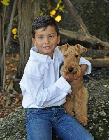 Young boy sitting outdoors with an Irish Terrier dog.