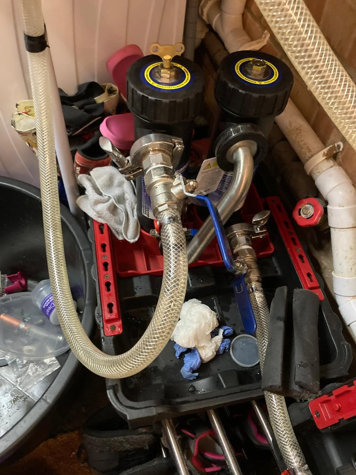 A plumbing work setup with hoses, valves, and tools on a workbench, including a water filter system, cleaning rags, and a plastic bottle.