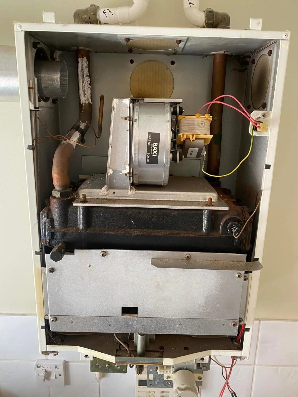 Interior view of an old furnace or boiler showing pipes, metal components, and wiring.