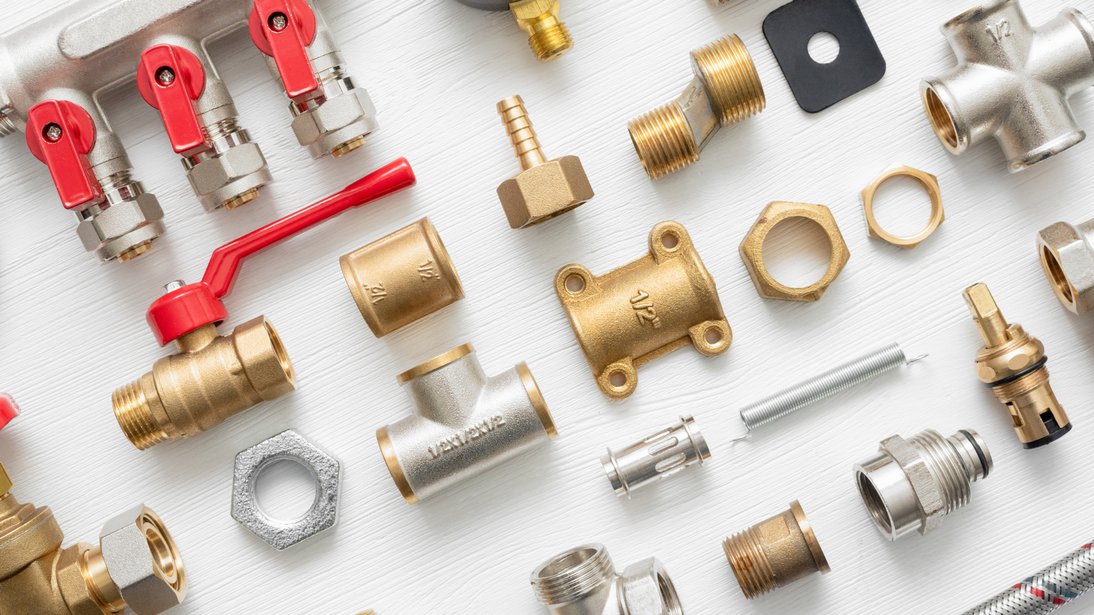 Various plumbing fittings and connectors, including valves, nuts, and pipe adapters, arranged on a white surface.