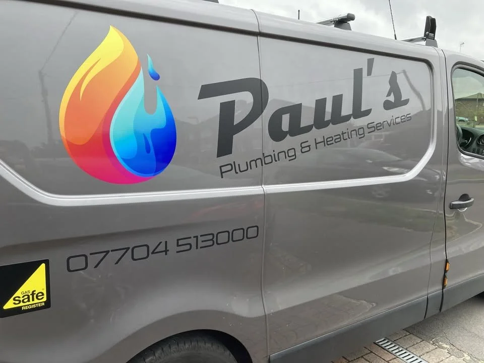 A gray service van with the logo of Paul's Plumbing & Heating Services, featuring a colorful water droplet and contact information.