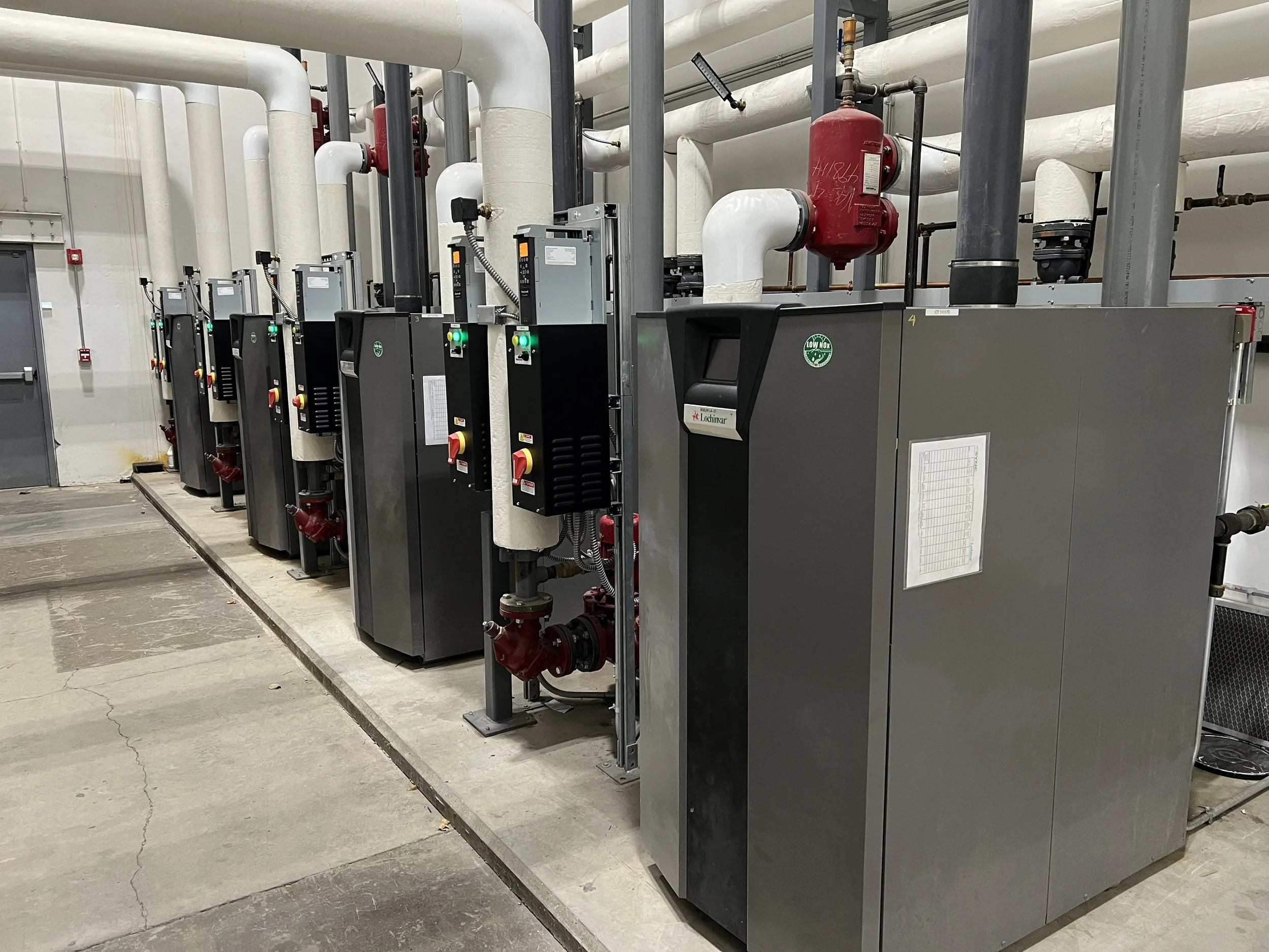 Industrial mechanical equipment with pipes, valves, and control units mounted on a concrete floor in an indoor facility.