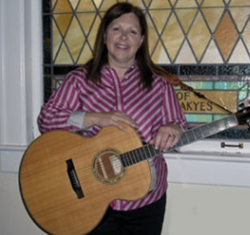 Woman holding an acoustic guitar in front of a stained glass window.