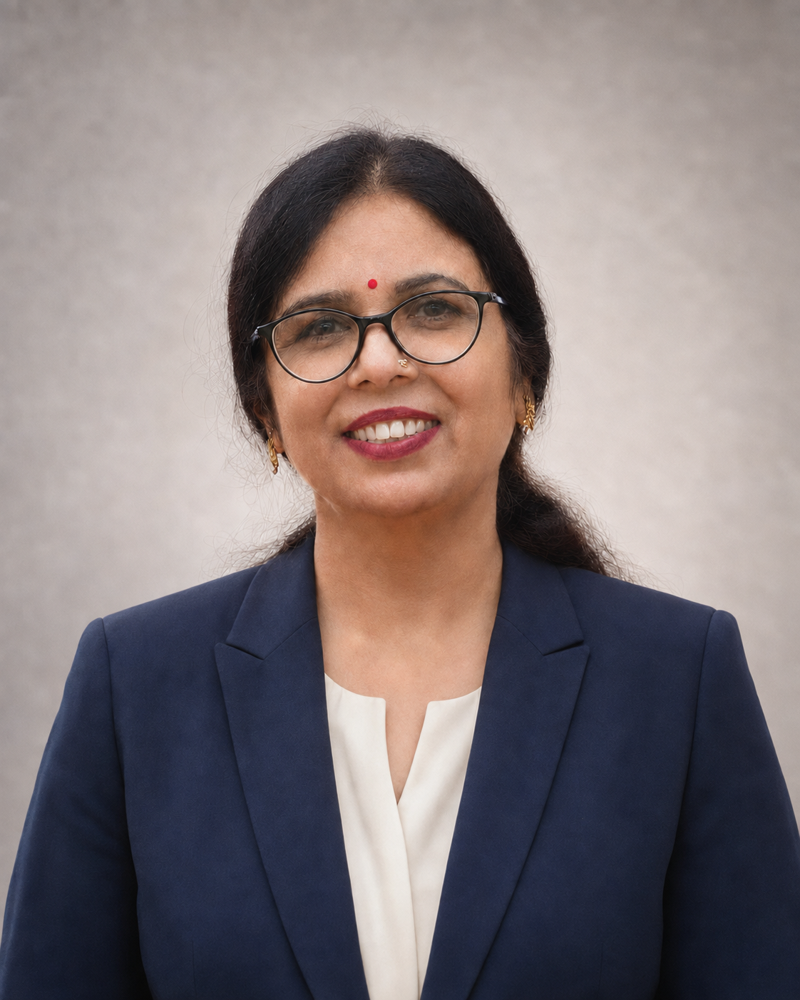 A professional woman with black hair, glasses, red lipstick, wearing a dark blue blazer and cream blouse, smiling against a neutral background.