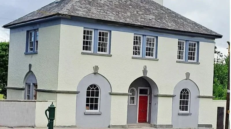 A two-story house with a textured light-colored exterior, blue window frames, and a red front door.
