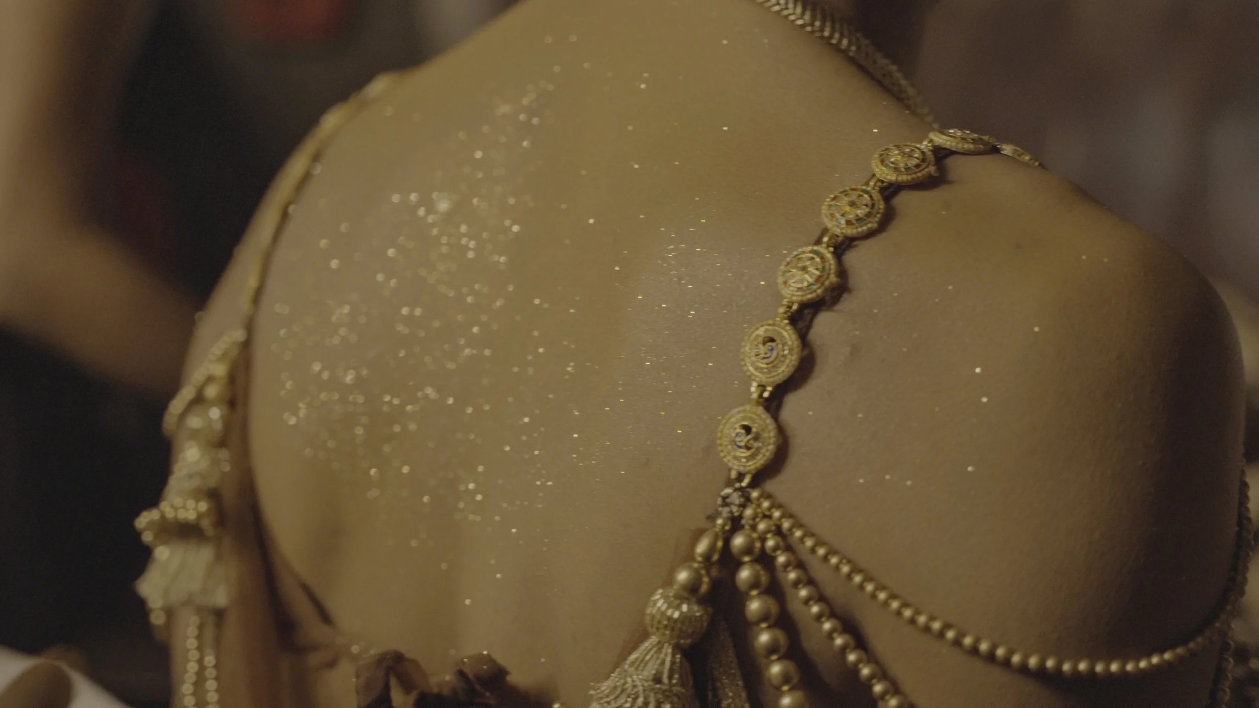 Close-up of a gold jewelry necklace on a beige surface with a glittery finish.