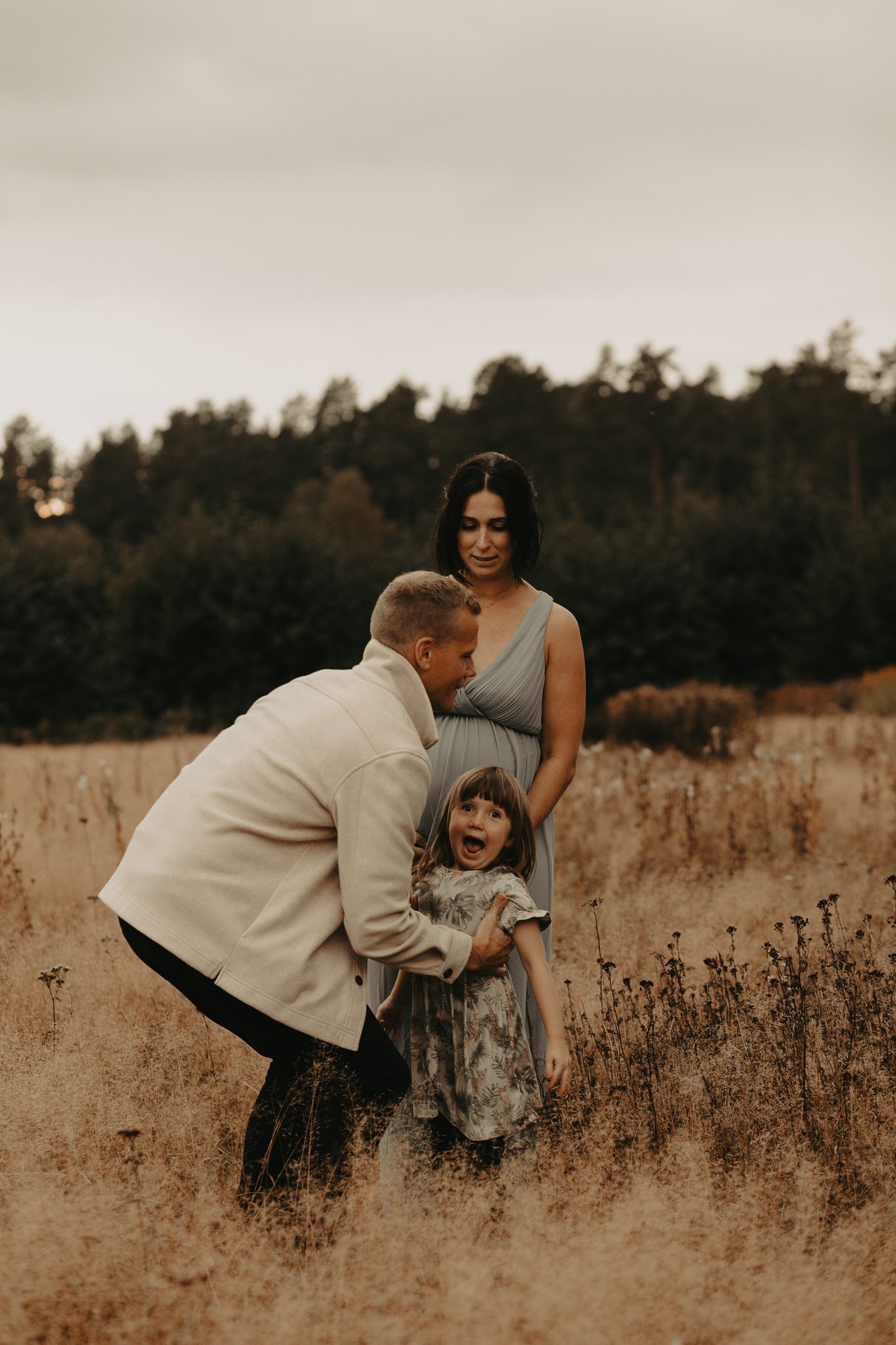 Familj i ett fält med torra växter, två vuxna och ett barn, under en molnig himmel