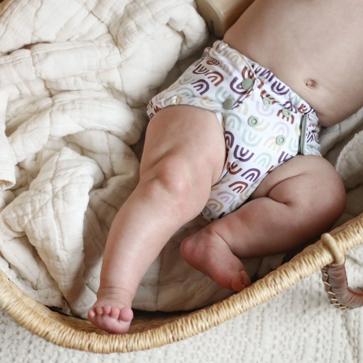 Close-up of a baby lying in a wicker basket on a soft blanket, wearing a colorful patterned diaper.