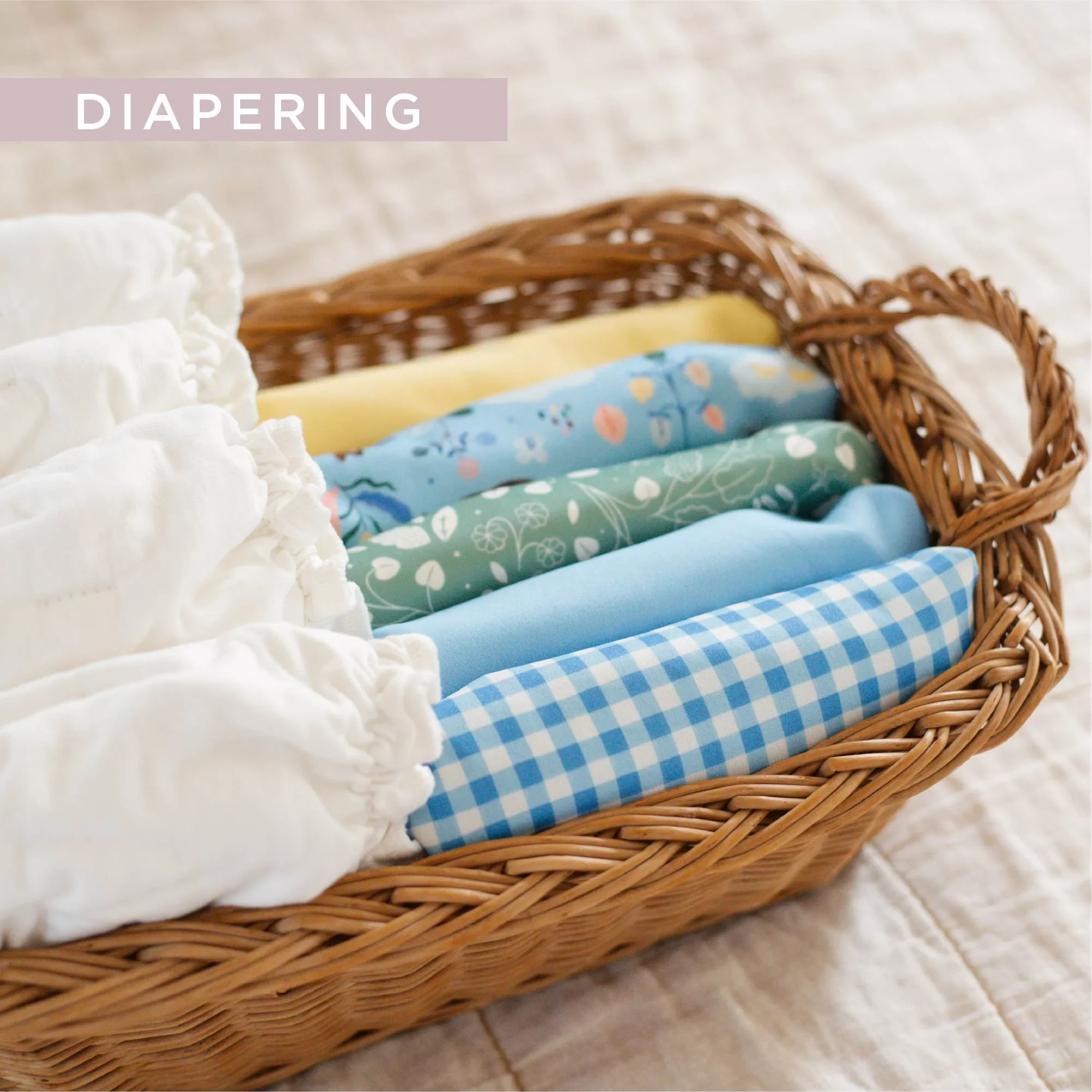 Close-up of a wicker basket filled with folded baby cloth diapers in various pastel colors with patterns.