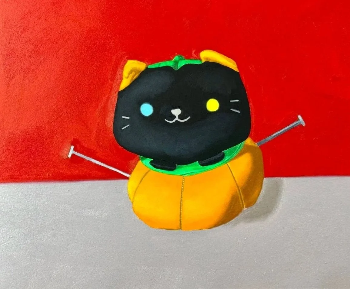 A stuffed black cat popping out of a stuffed orange pumpkin, placed against a red wall.