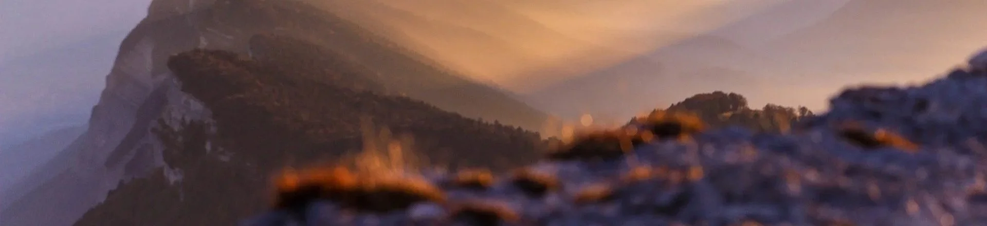 Close-up of a mountain landscape during sunset, with rocky terrain in the foreground and fog-covered mountains in the background.