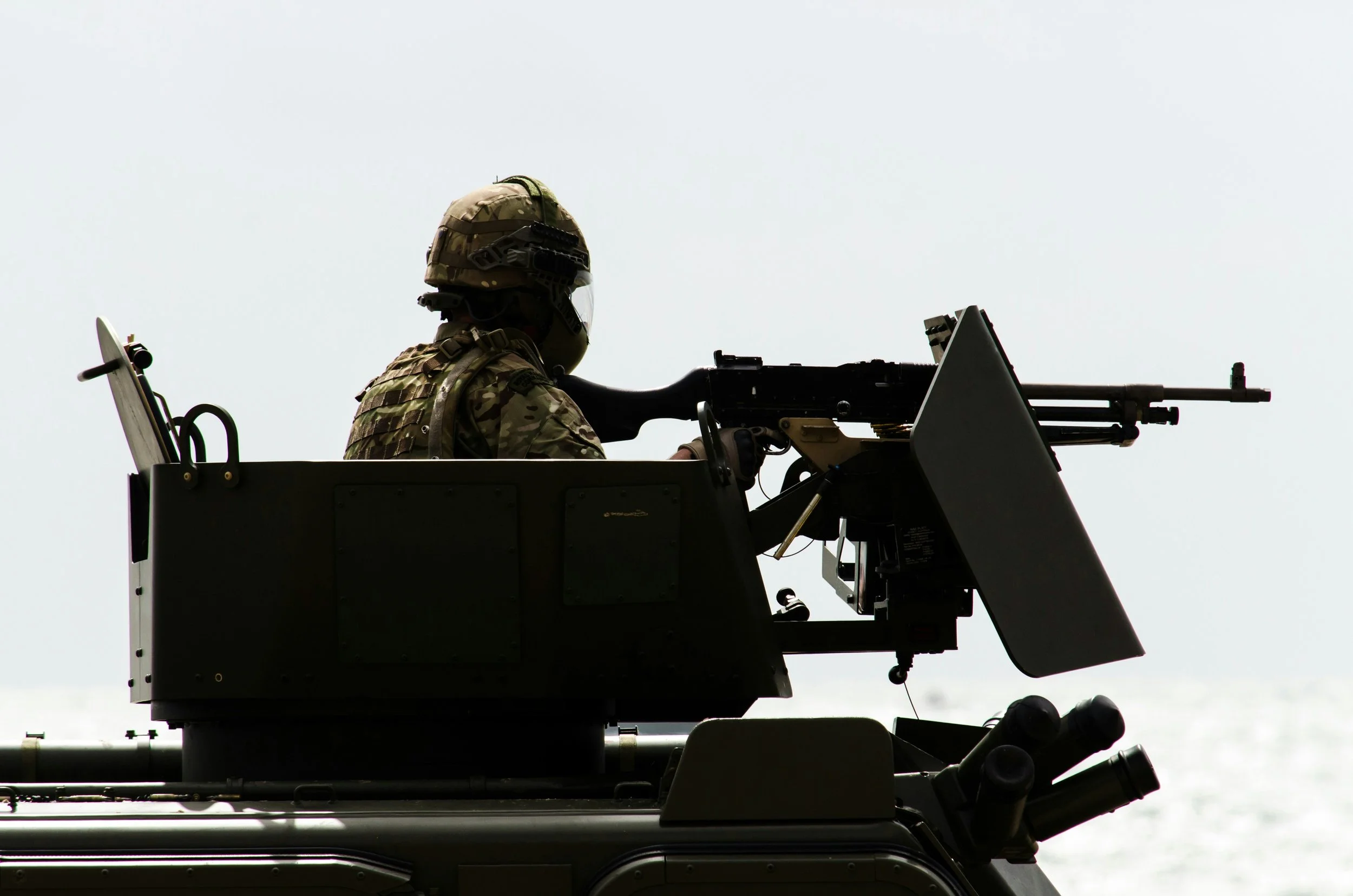 A soldier in camouflage uniform and helmet operating a mounted machine gun on a military vehicle.