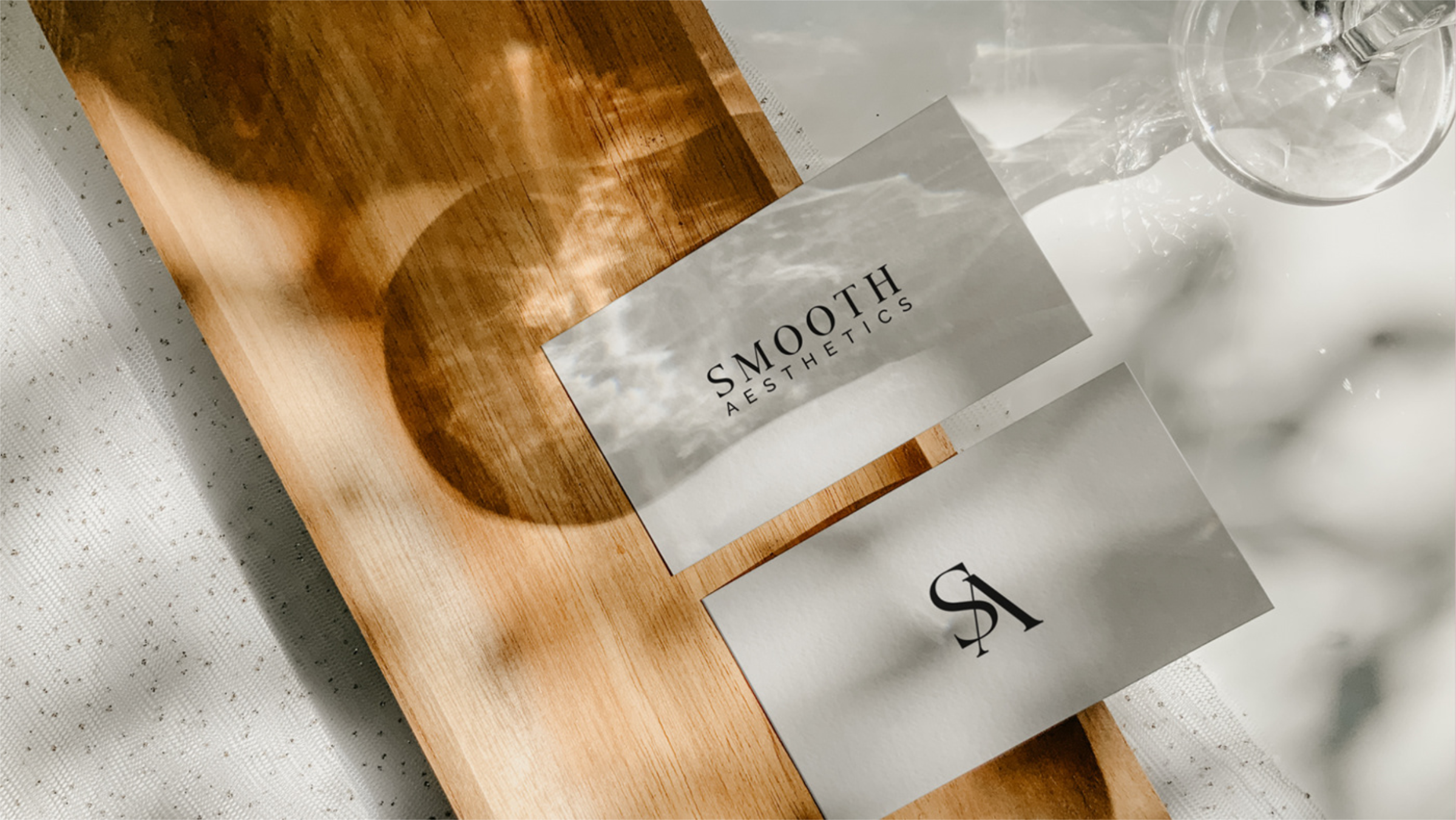 Close-up of a wooden board with a metallic label reading "SMOOTH AESTHETICS" and partially visible paper with scientific or mathematical symbols. A glass water pitcher with a plastic cover is in the background.