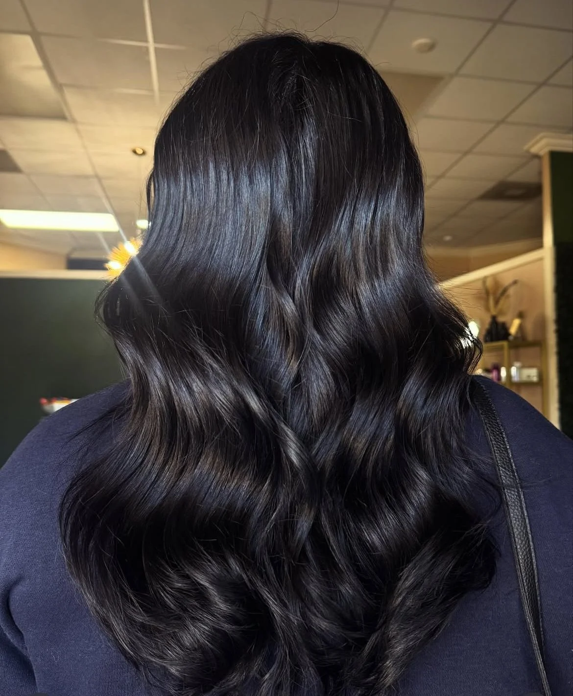 Back of a woman with long, dark, shiny, wavy hair.