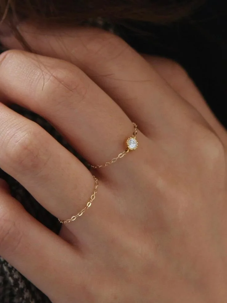 A hand with a gold chain ring featuring a small diamond or gemstone.