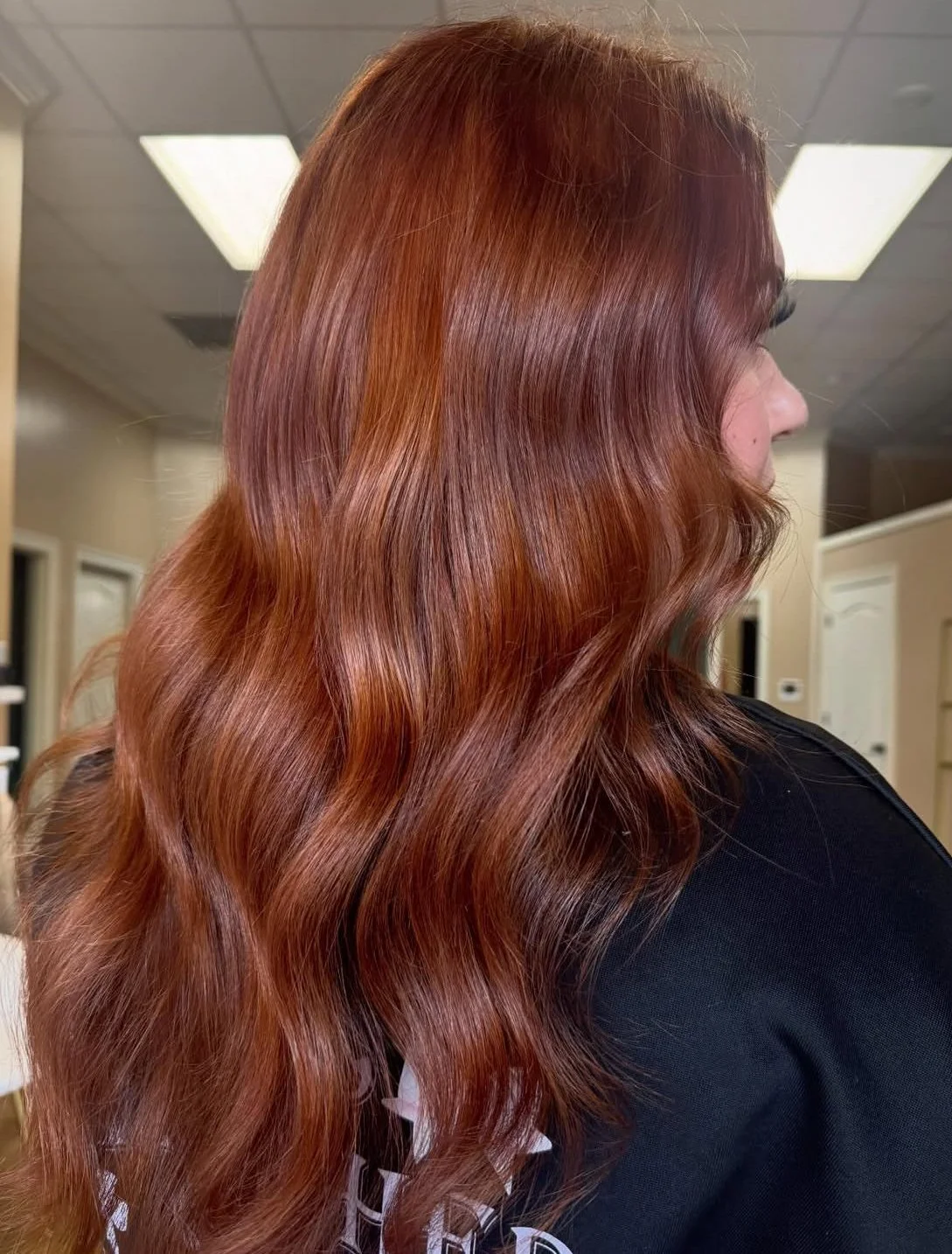 Side view of a woman with long, wavy red hair in a salon.