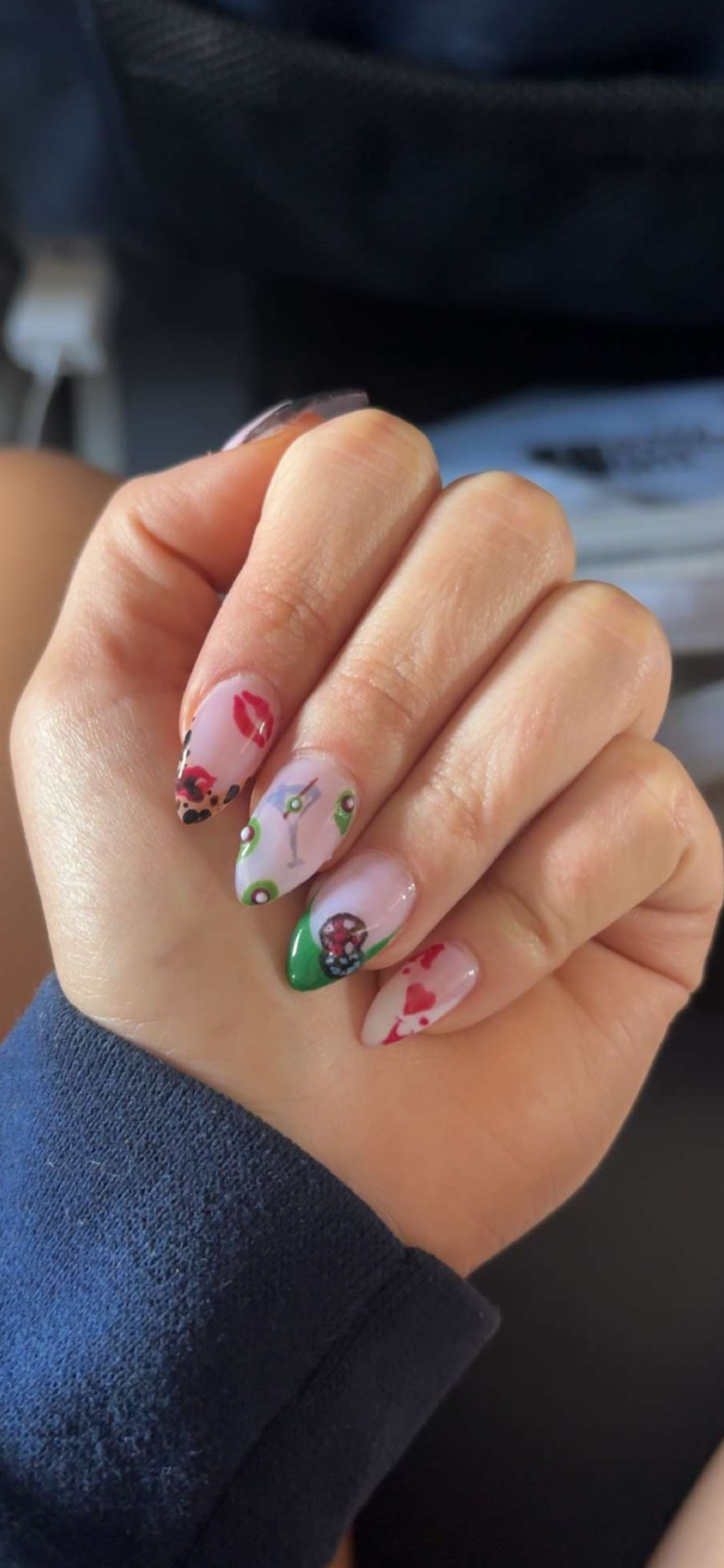 Close-up of a hand with decorated fingernails, featuring various colorful designs including hearts, flowers, and abstract patterns.