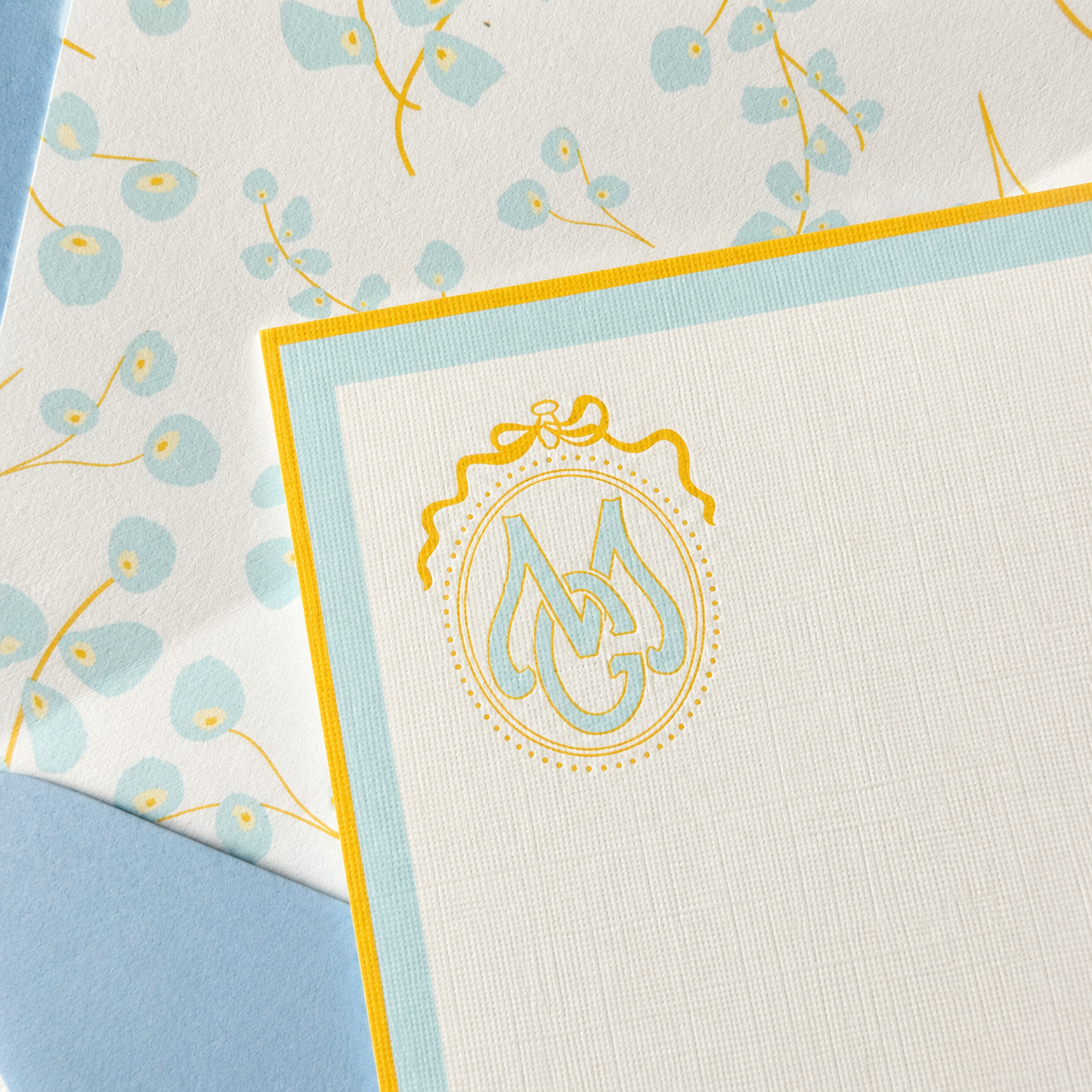 Personalized ivory stationery with a pale blue and gold monogram, coordinating floral envelope liner, and light blue envelope.
