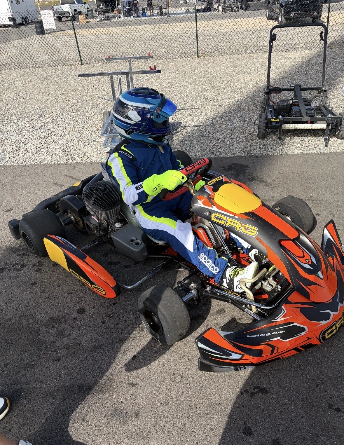 A person in racing gear sitting in a go-kart at a racetrack.