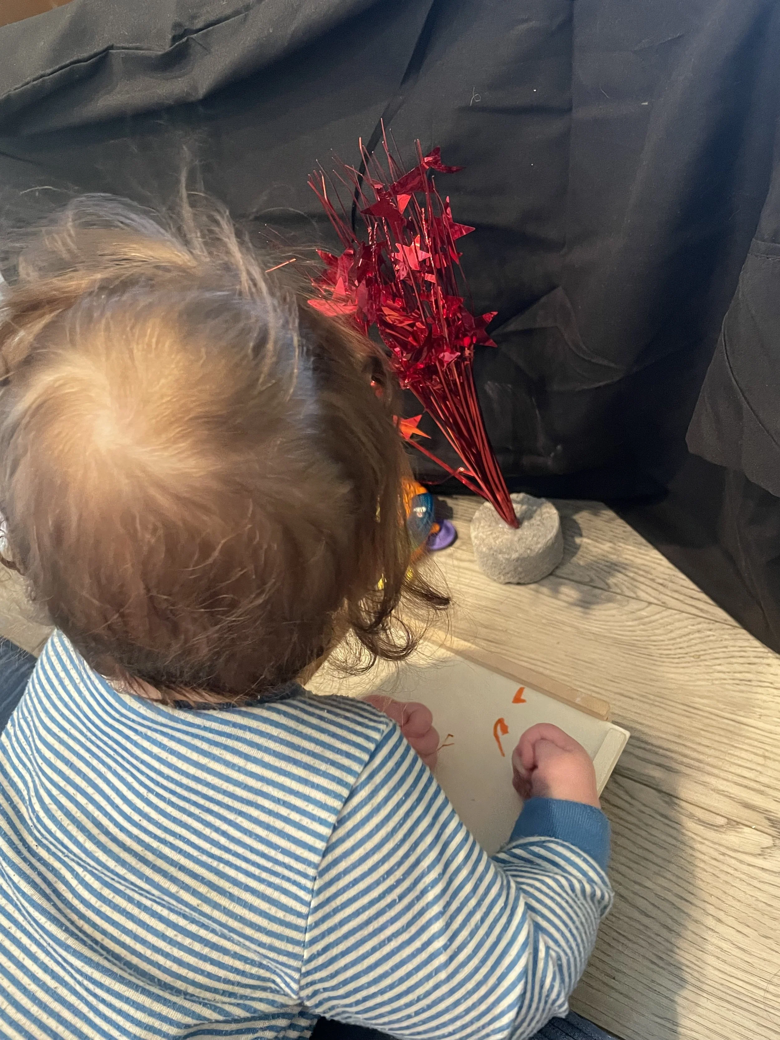 Baby doing tummy time while looking at a shiny red table decoration set against a black sheet. 