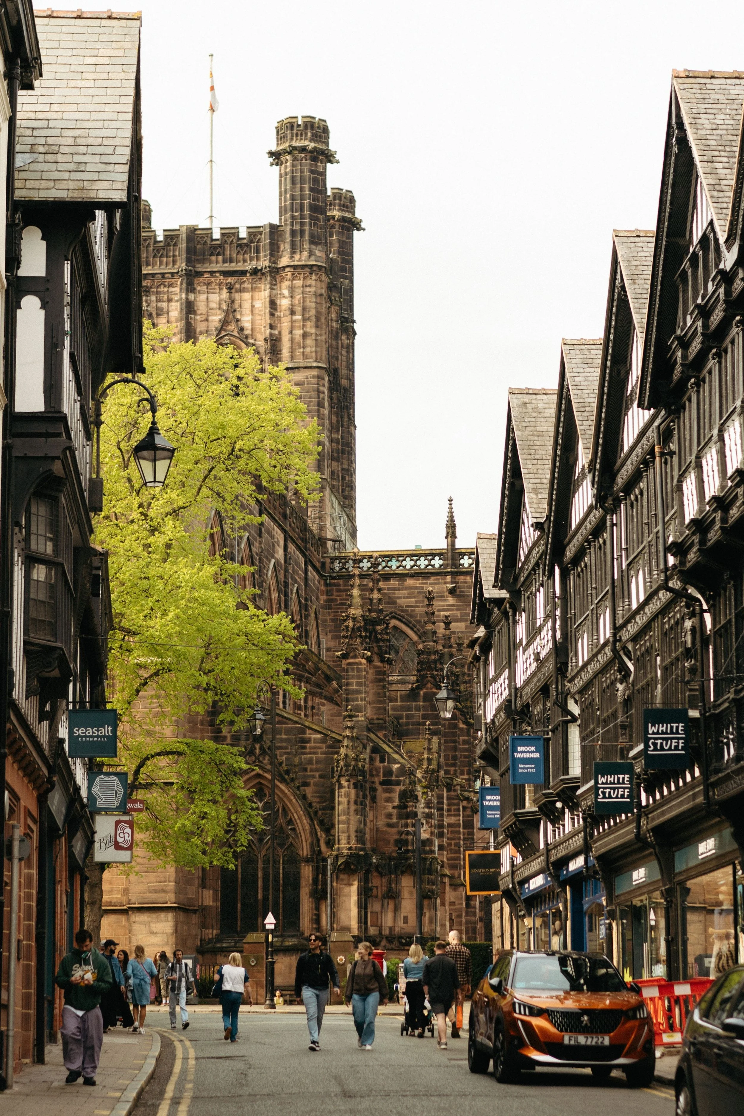 Historic Edinburgh street with Gothic cathedral, half-timbered buildings, shops, pedestrians, and an orange taxi