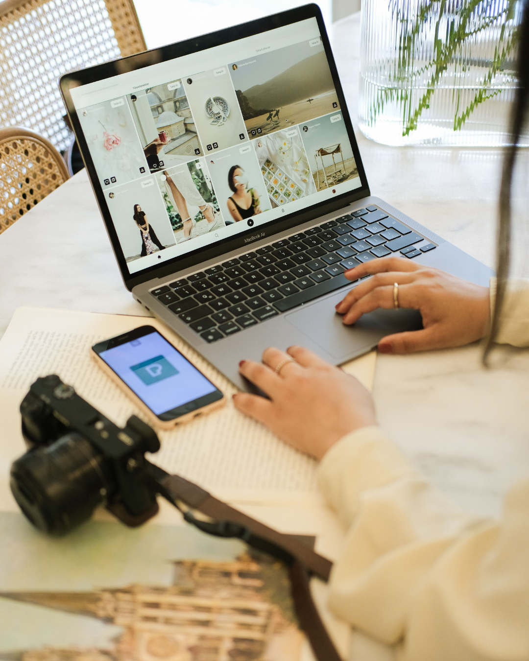 Person browsing a photo-sharing website on a laptop beside a smartphone and DSLR camera.