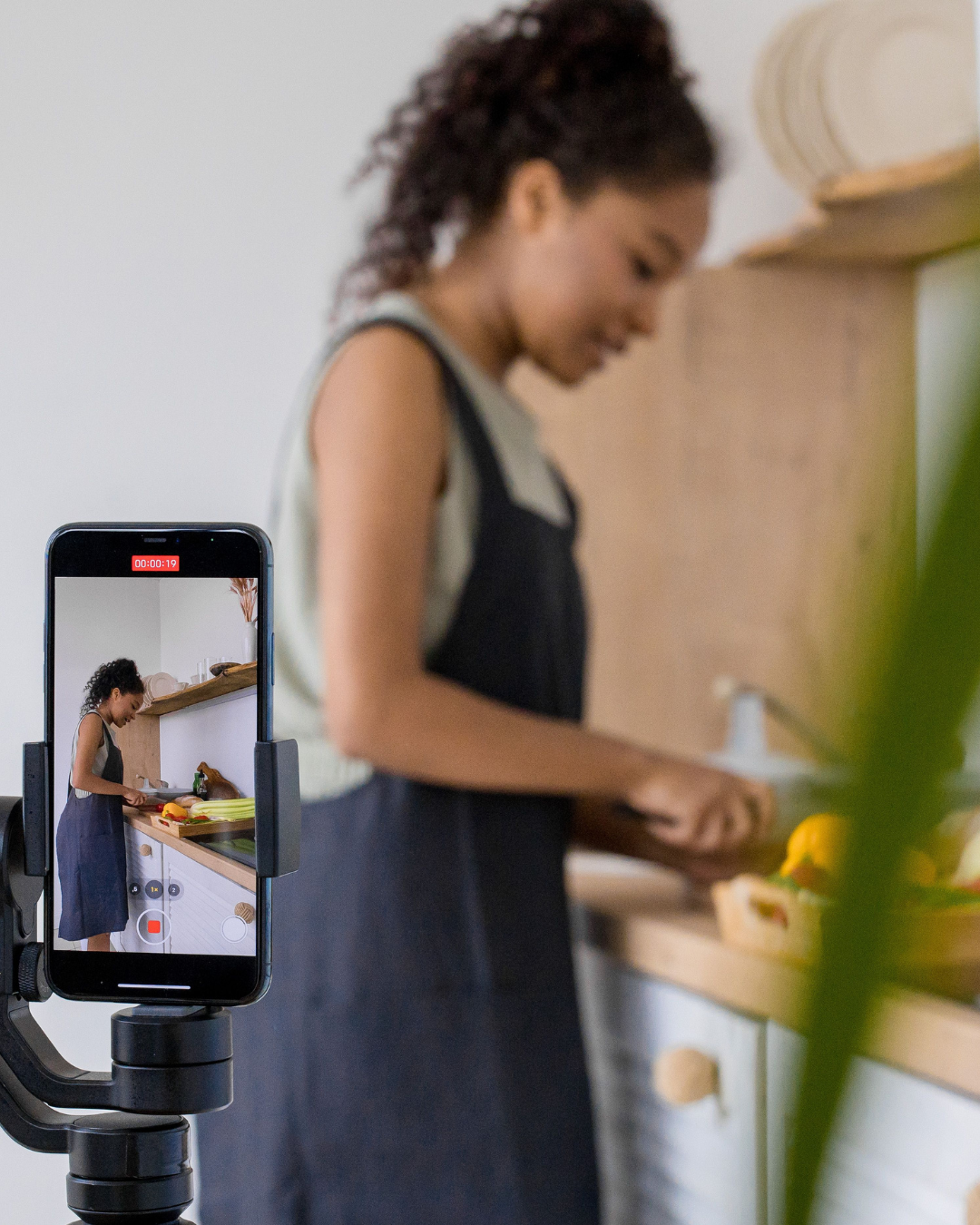 Woman filming herself cooking in a kitchen with a smartphone on a gimbal