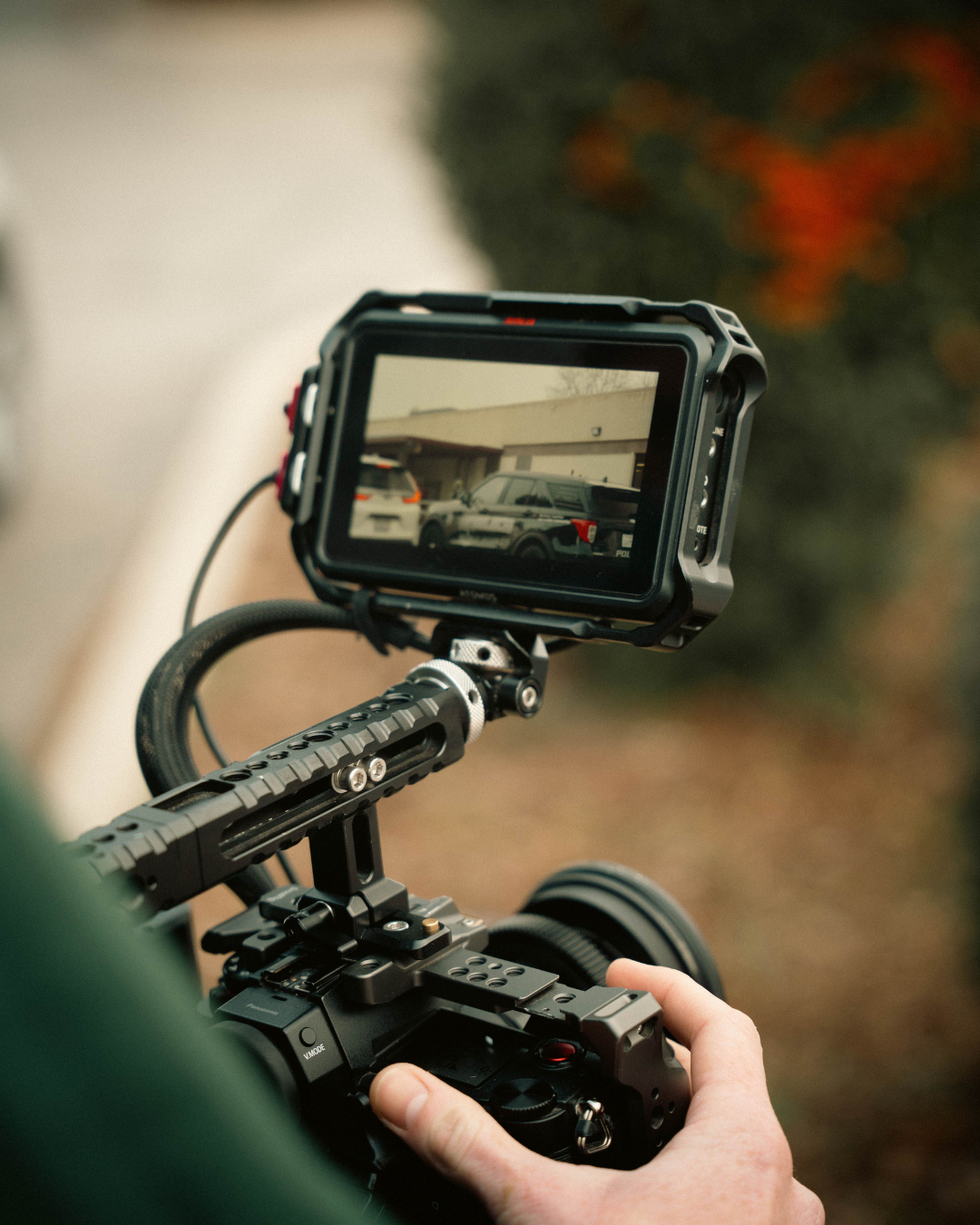 Filmmaker operating a professional video camera with an external monitor showing parked cars