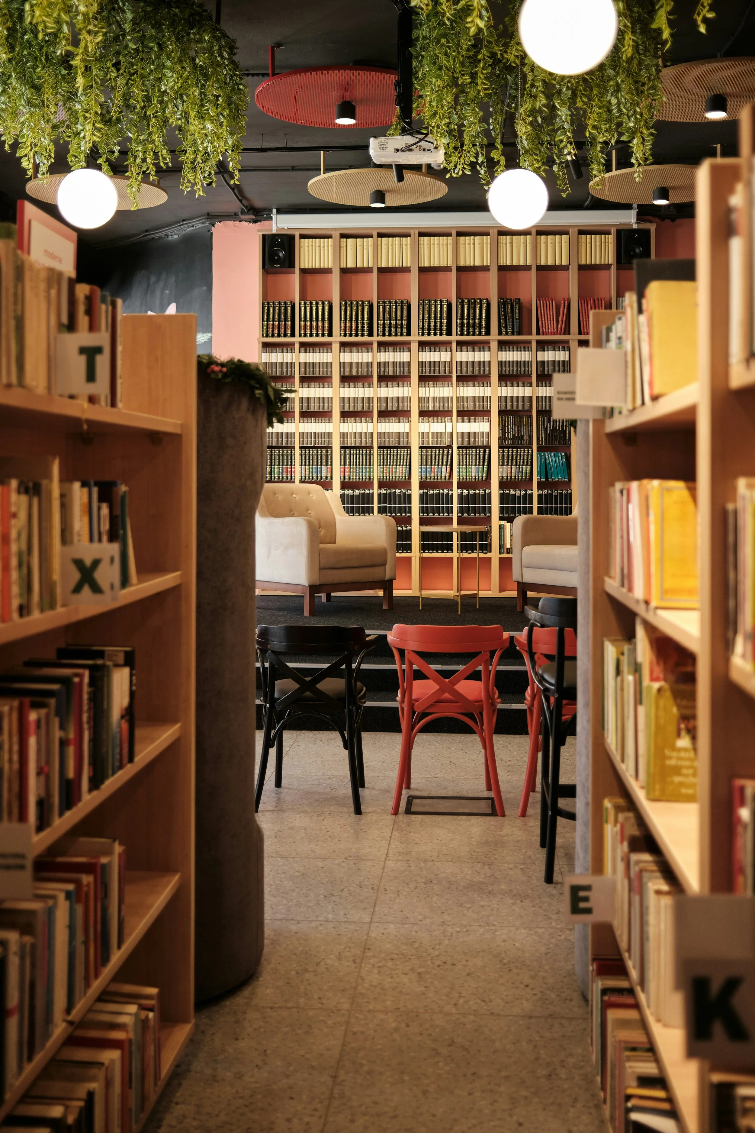 Blick durch Bücherregale in eine gemütliche Leseecke mit zwei Sesseln und einem Bücherregal im Hintergrund.