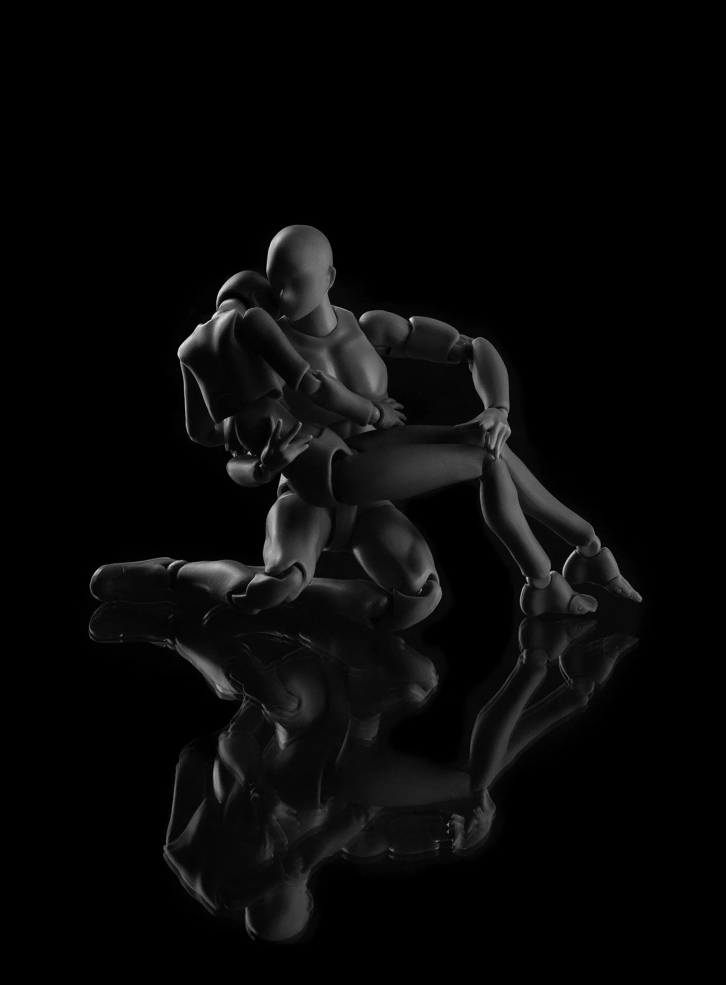 Black and white photo of a humanoid robot holding a smaller robot in its arms, with their reflections visible on a shiny surface below.