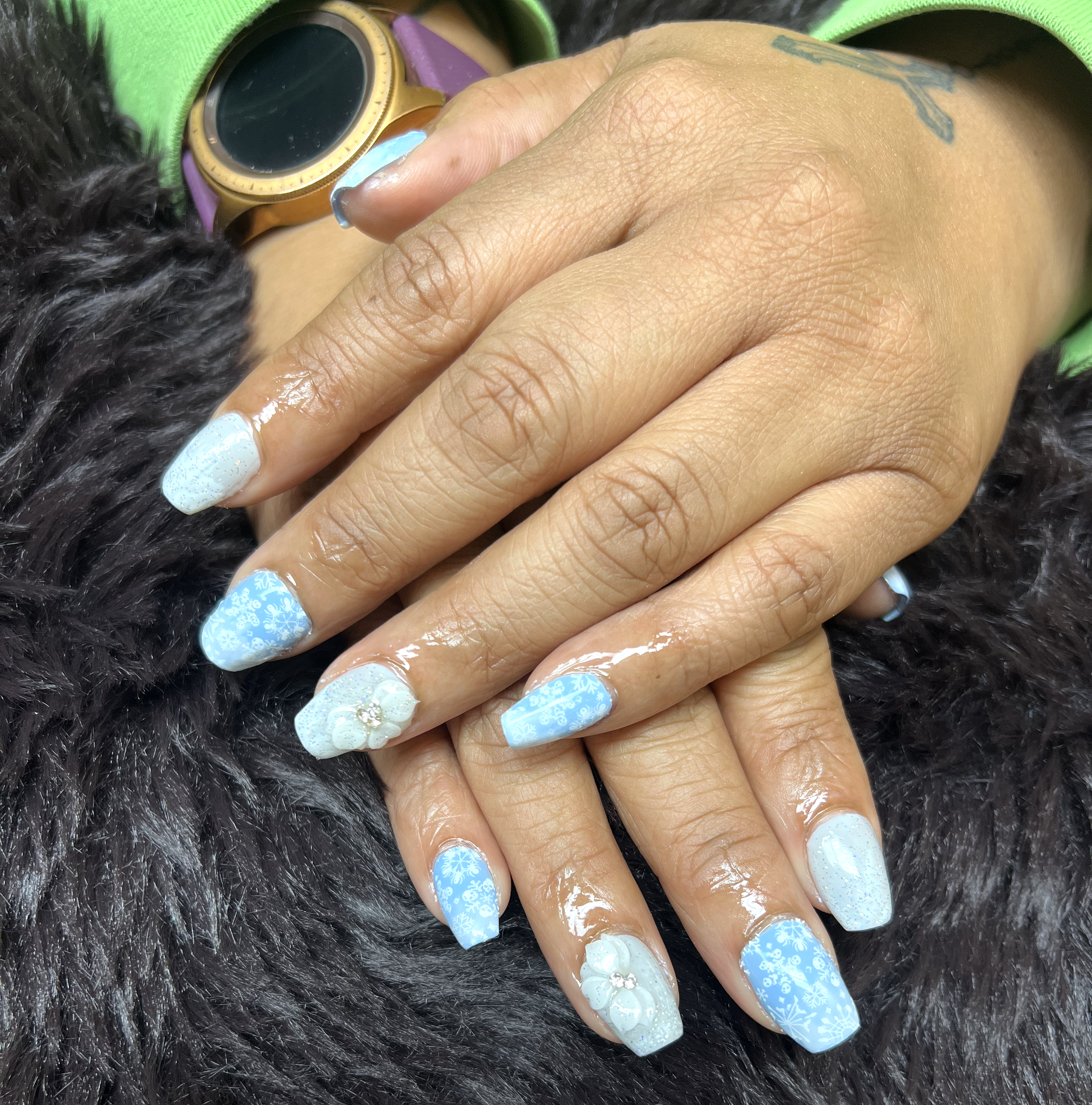 Close-up of a hand with nails painted in winter themes, holding a person's wrist displaying a smartwatch, with a background of dark fur.
