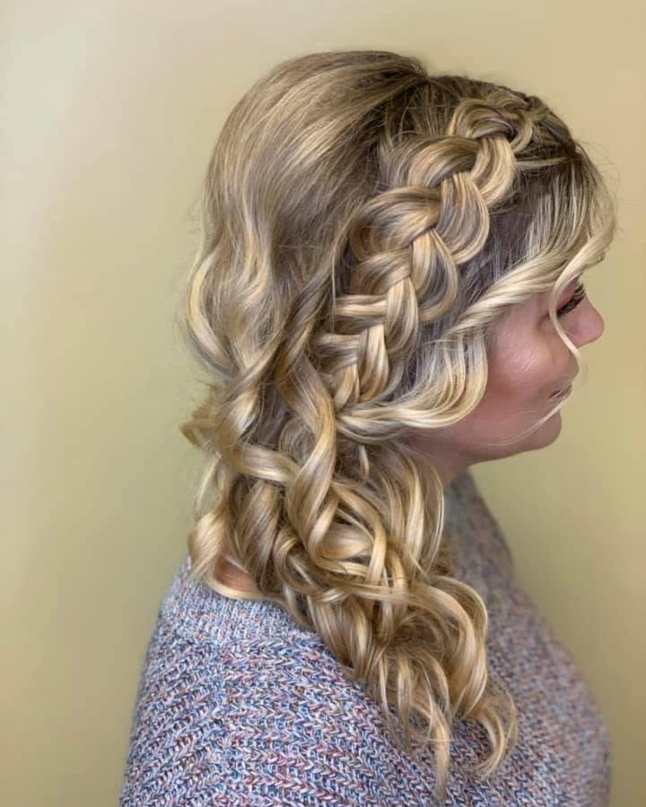 Woman with blonde hair styled in loose curls with a side braid on top.
