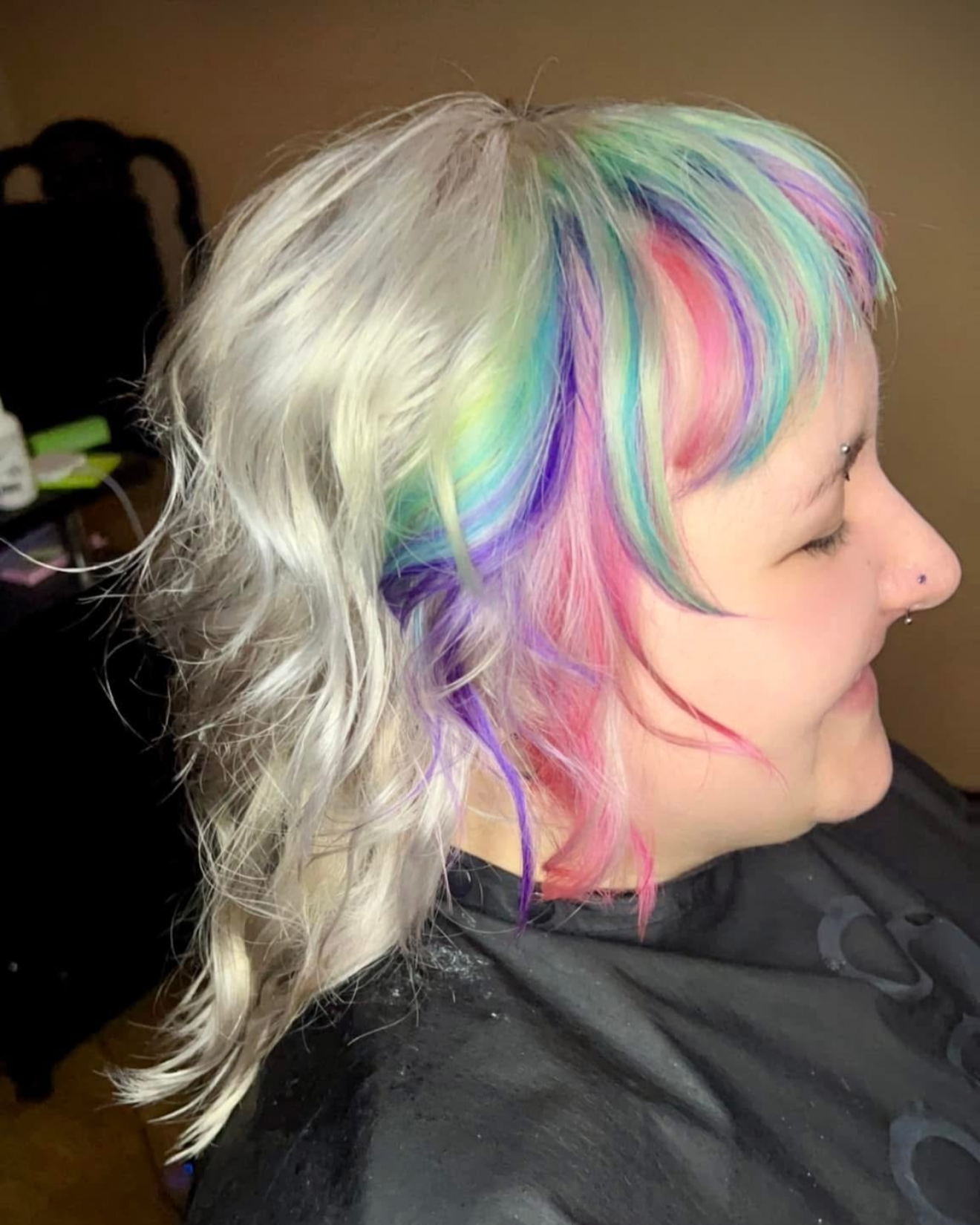 A woman with blonde hair having sections dyed in pastel rainbow colors, including green, blue, purple, pink, and peach.