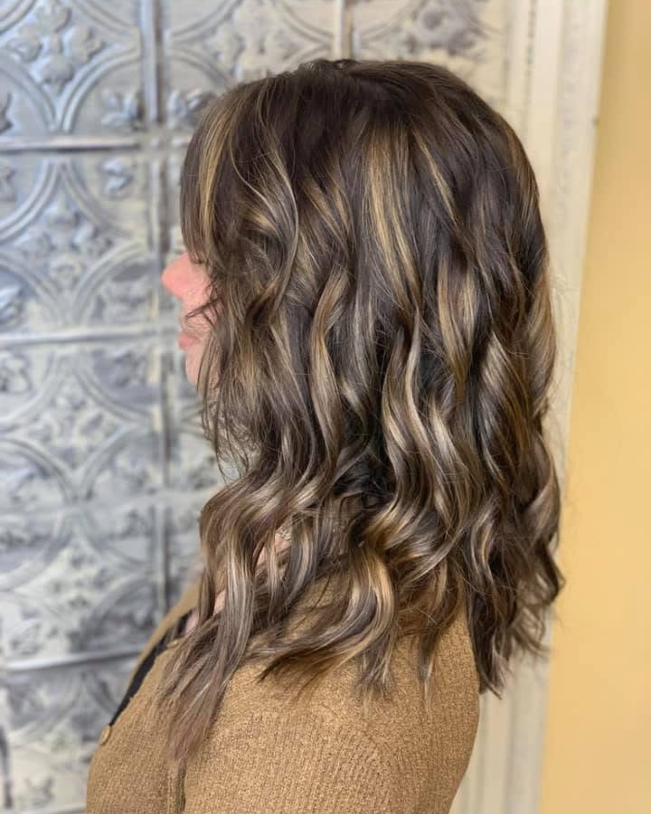 Side view of a woman with medium-length hair styled in loose, dark brown curls with blonde highlights.