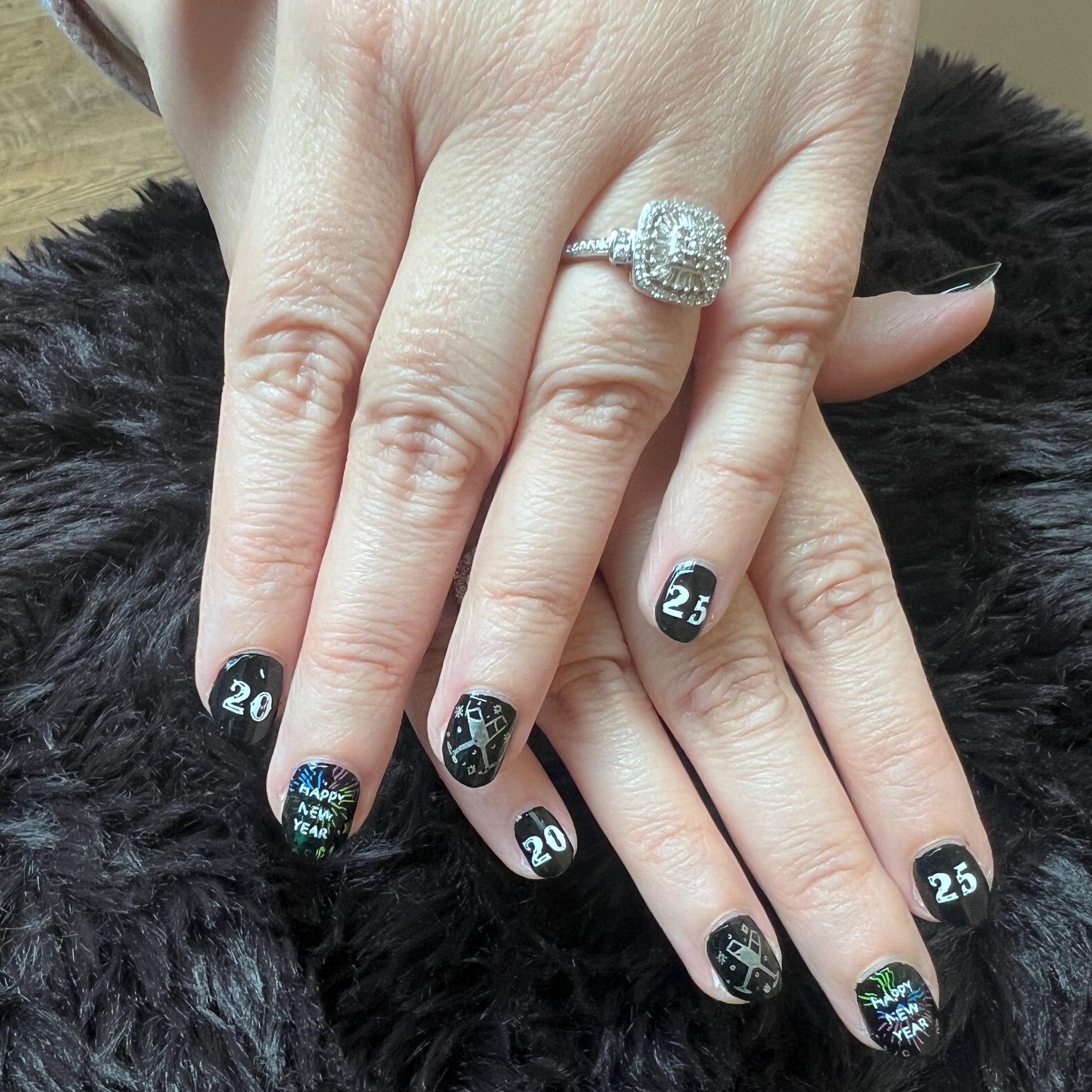 Close-up of a person's hand with nails painted black, decorated with New Year-themed graphics and numbers representing the year 2020, resting on a black furry surface.