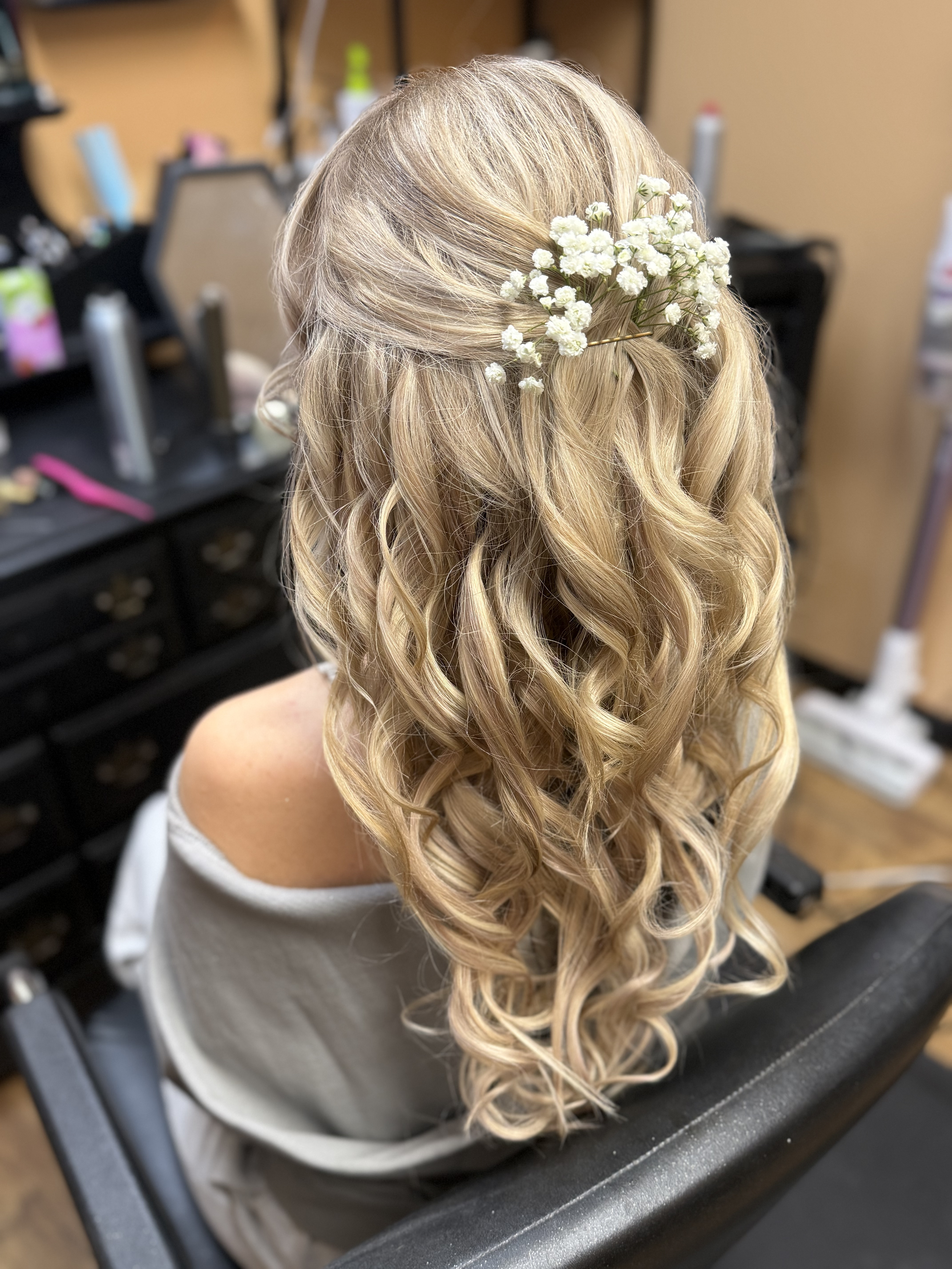 A woman's blonde curly hair styled with a floral hair accessory in a hair salon.