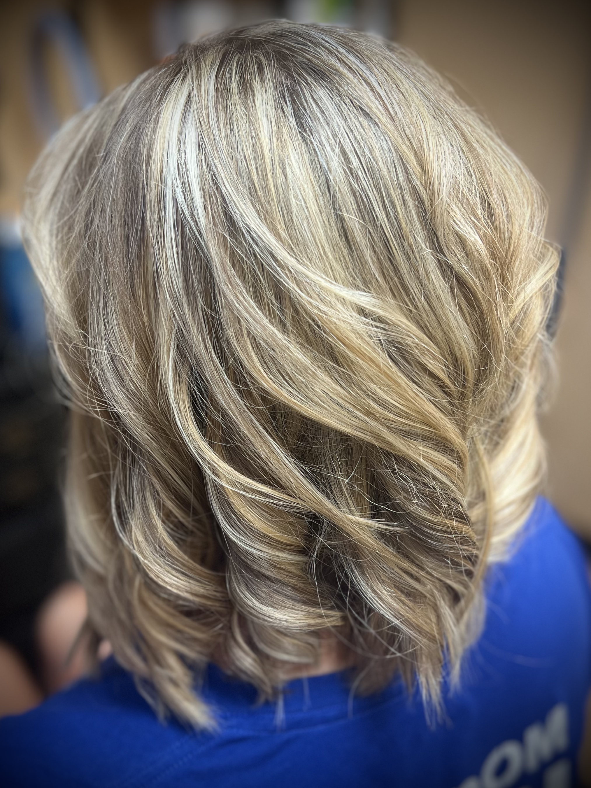 Close-up of a person's blonde hair styled in loose waves, with a blurred background.