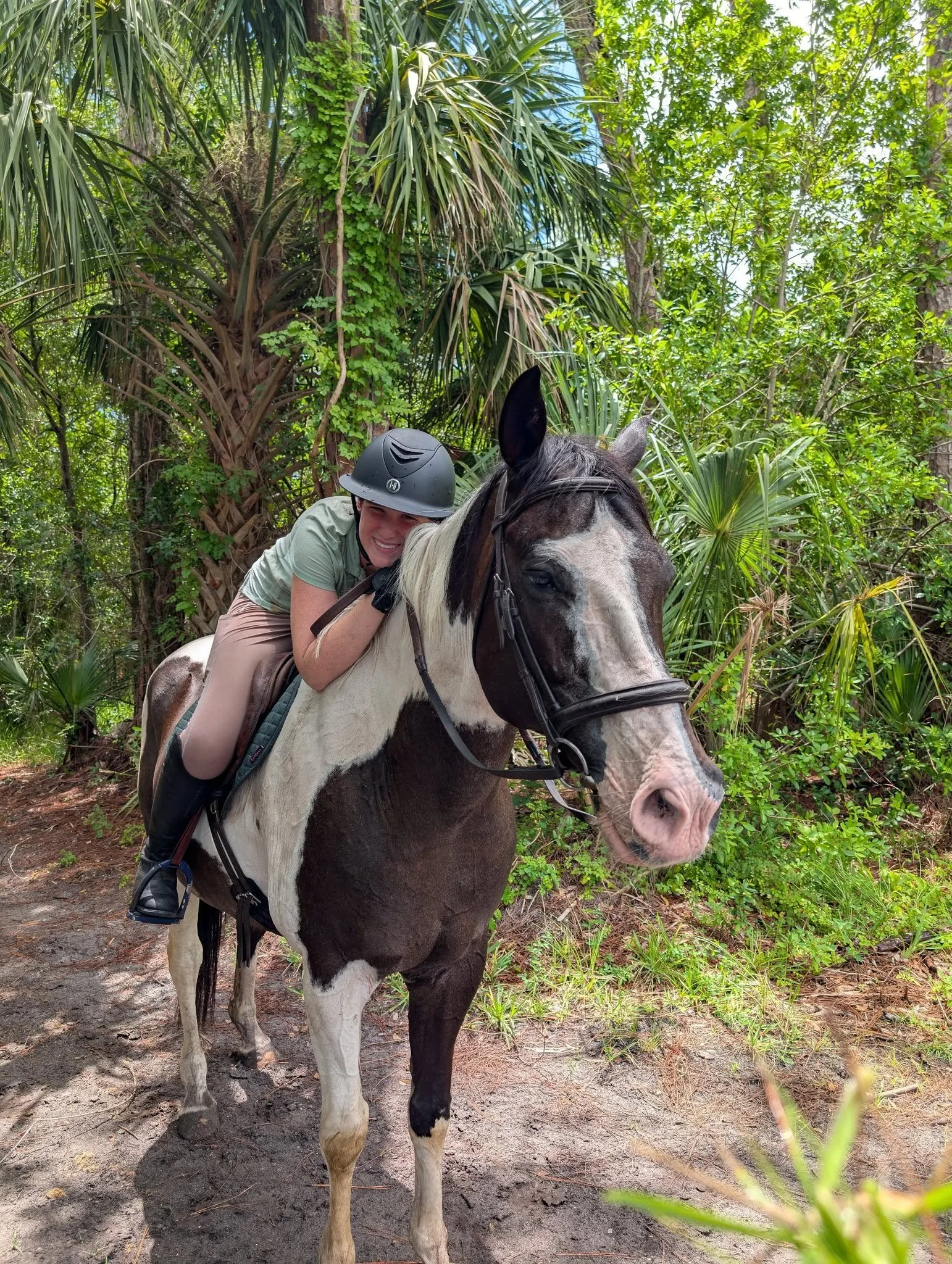 A woman riding a black and white horse in a forest with lush green trees and plants.