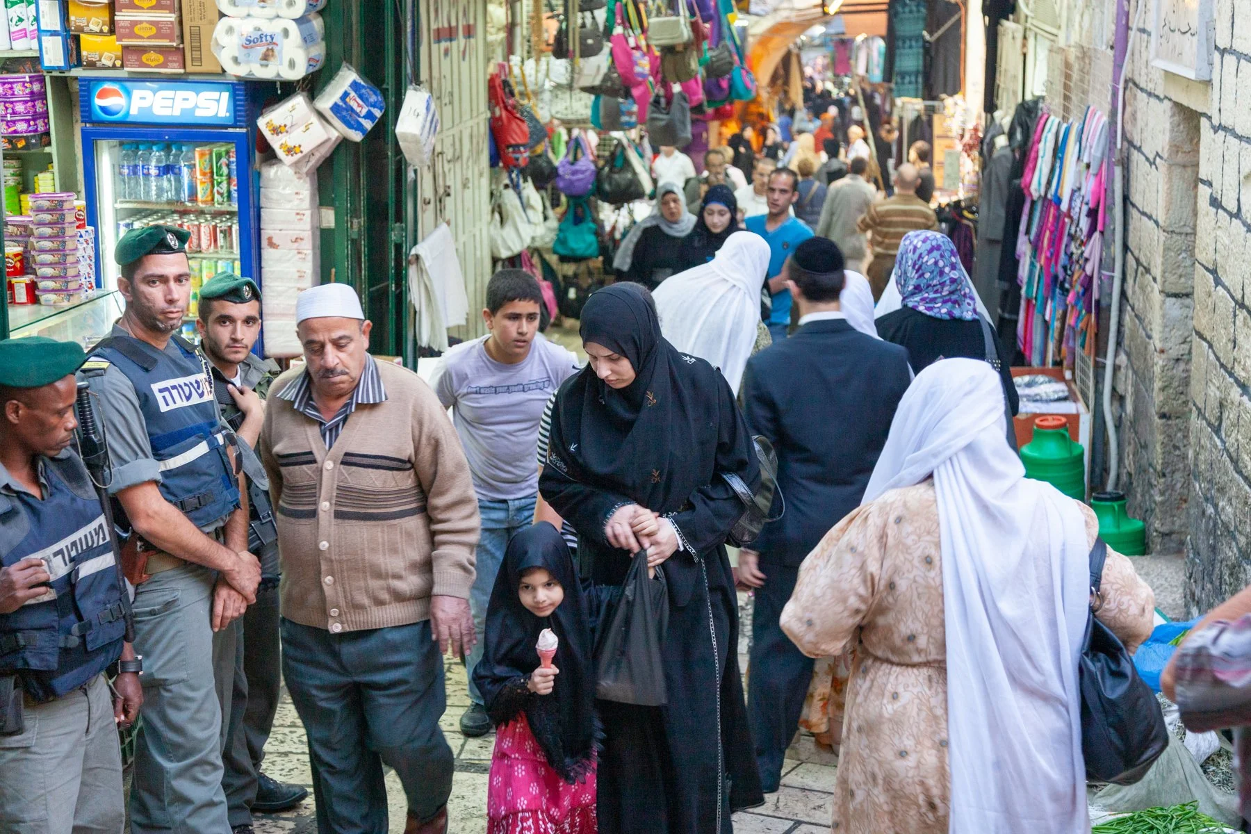 Crowded market street with shoppers, families and security personnel in Jerusalem’s Old City.