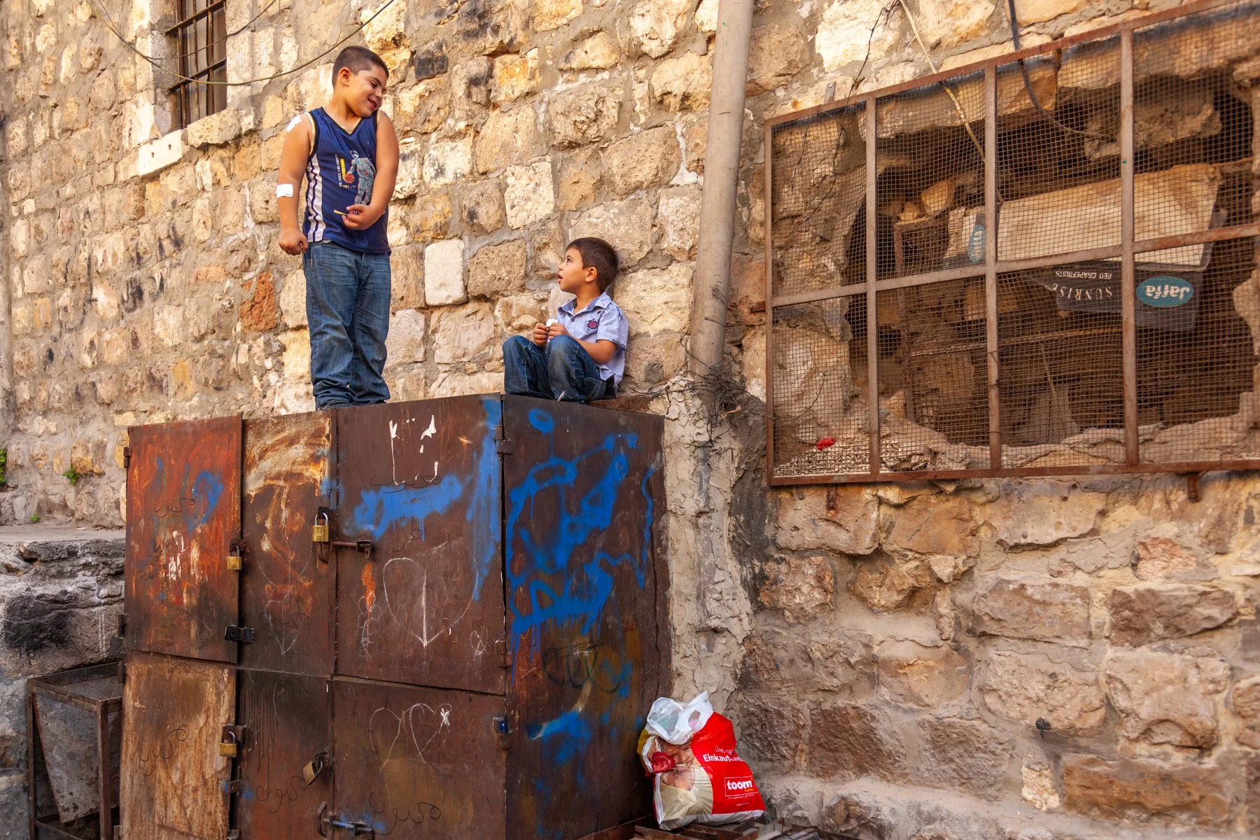 Two boys standing on stacked metal containers in a residential area of Jerusalem’s Old City.