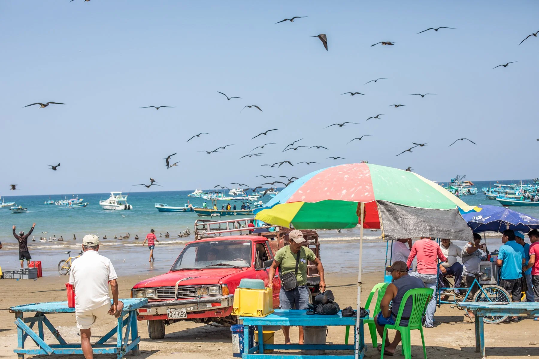 Fishing boats gather offshore while fishermen, vendors and visitors prepare for another morning at the beach fish market in Puerto López on Ecuador’s Pacific coast. Frigatebirds circle above the shoreline as the day’s catch begins to arrive.