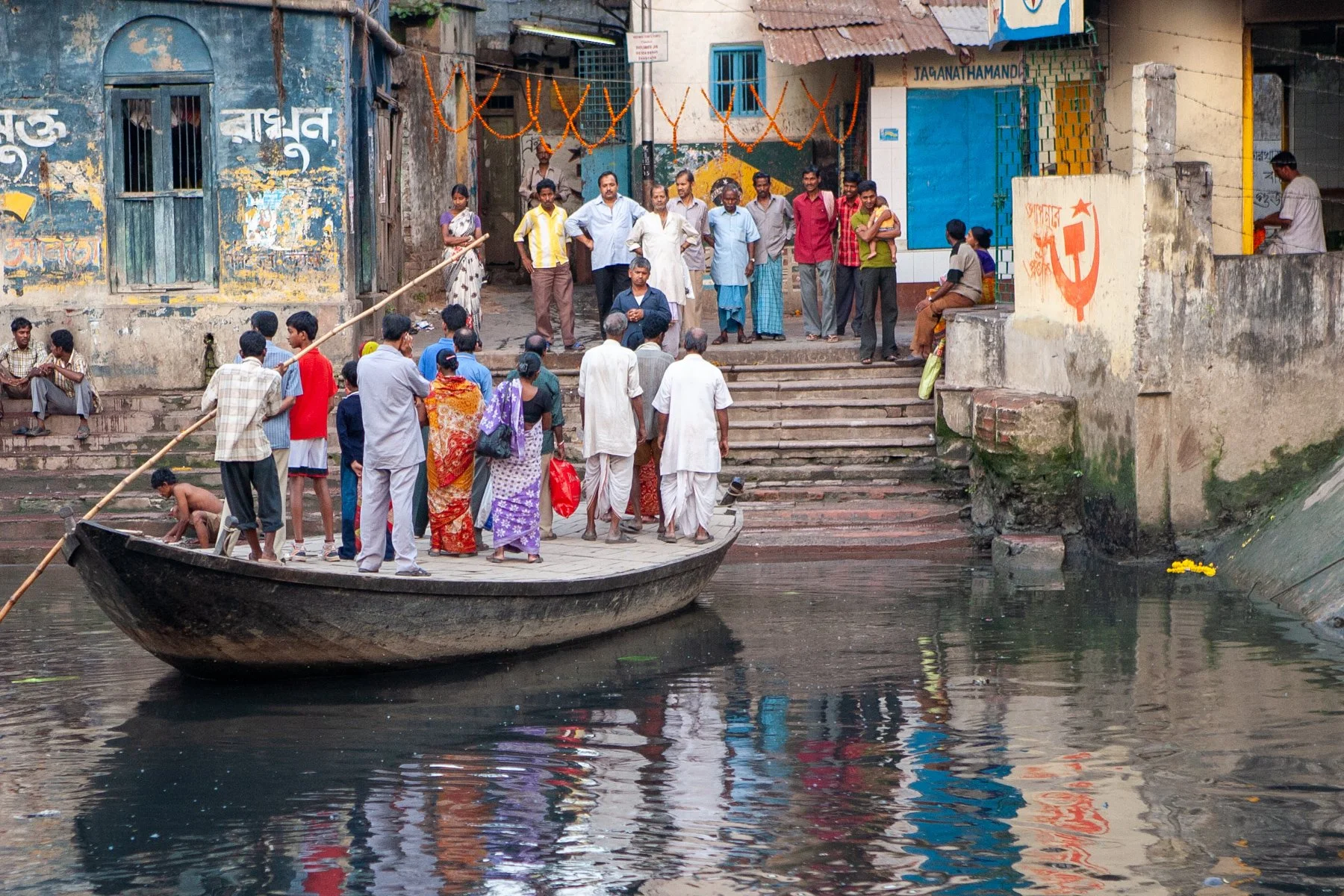 Residents cross a narrow canal by wooden boat in a residential neighbourhood of Kolkata, West Bengal, India. Small ferries remain an important part of daily transport, connecting communities separated by waterways.