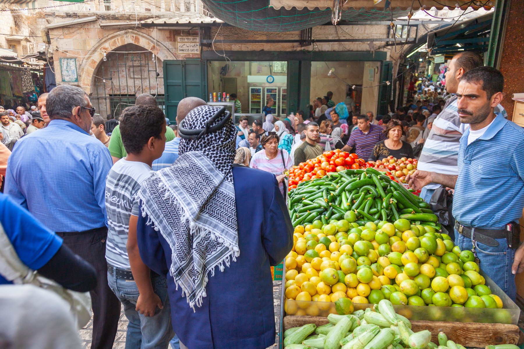 A man wearing a traditional keffiyeh walks past vegetable stalls in a narrow market street in the Old City of Jerusalem, Israel, 2010.