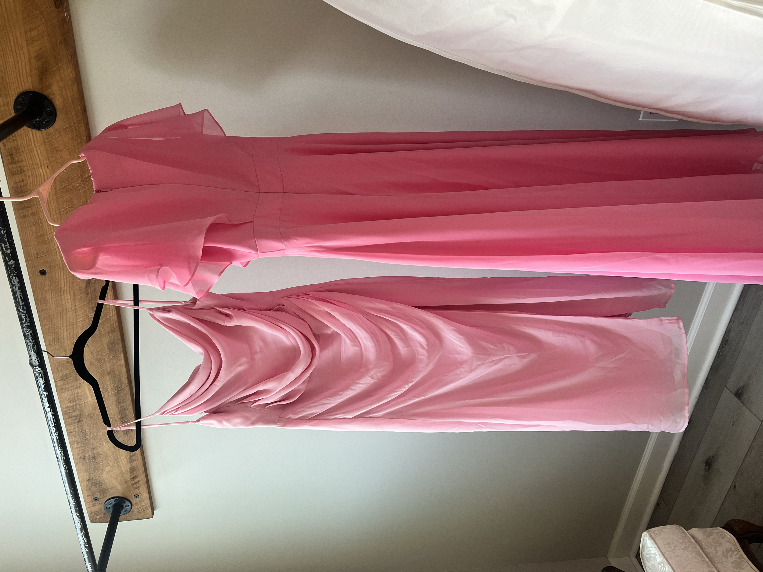 Pink satin dress hanging on a pink hanger mounted on a wooden shelf attached to a gray wall.