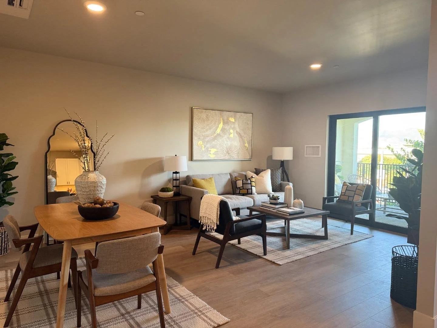 Living room with a beige sofa, black and wooden coffee table, armchair, artwork on the wall, and sliding glass door leading to balcony with outdoor balcony furniture.